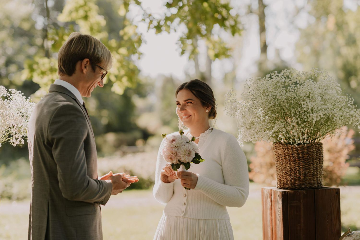 Elegant wedding decor with white floral arrangements on wooden pillars in a garden setting.