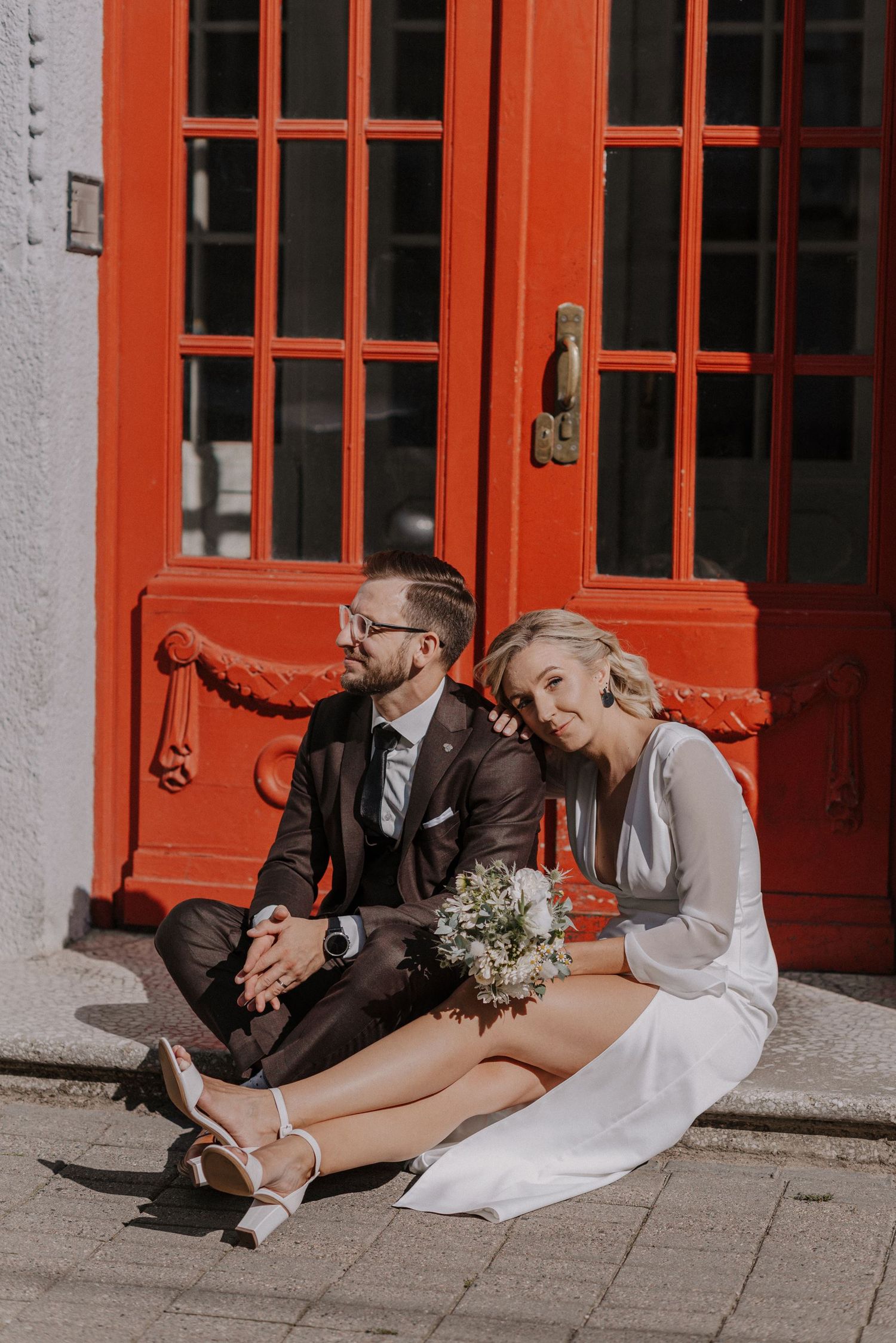 Candid wedding photos of a couple sitting and laughing together by bright red doors.