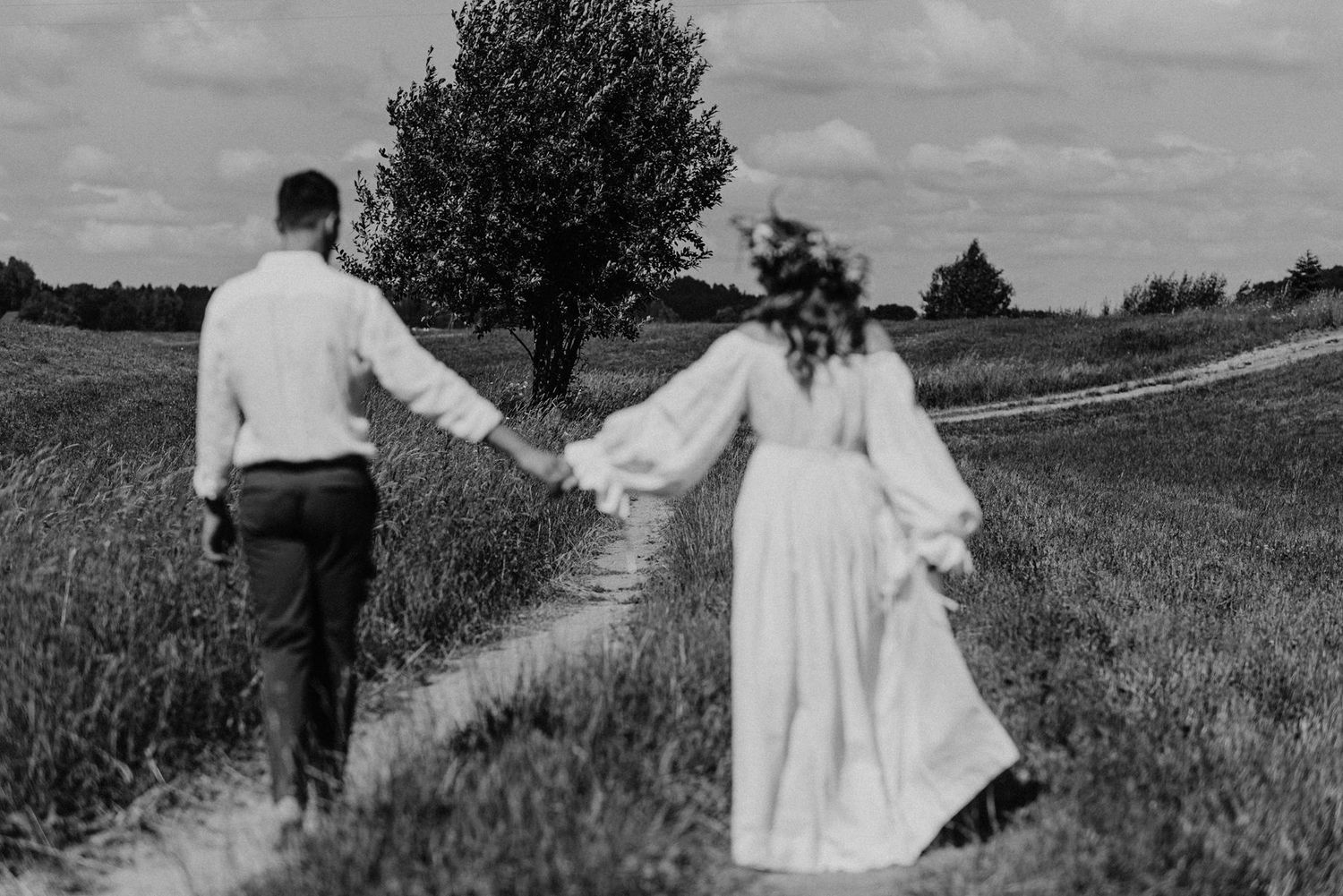 Black and white photo of newlyweds walking along a rural path through fields.
