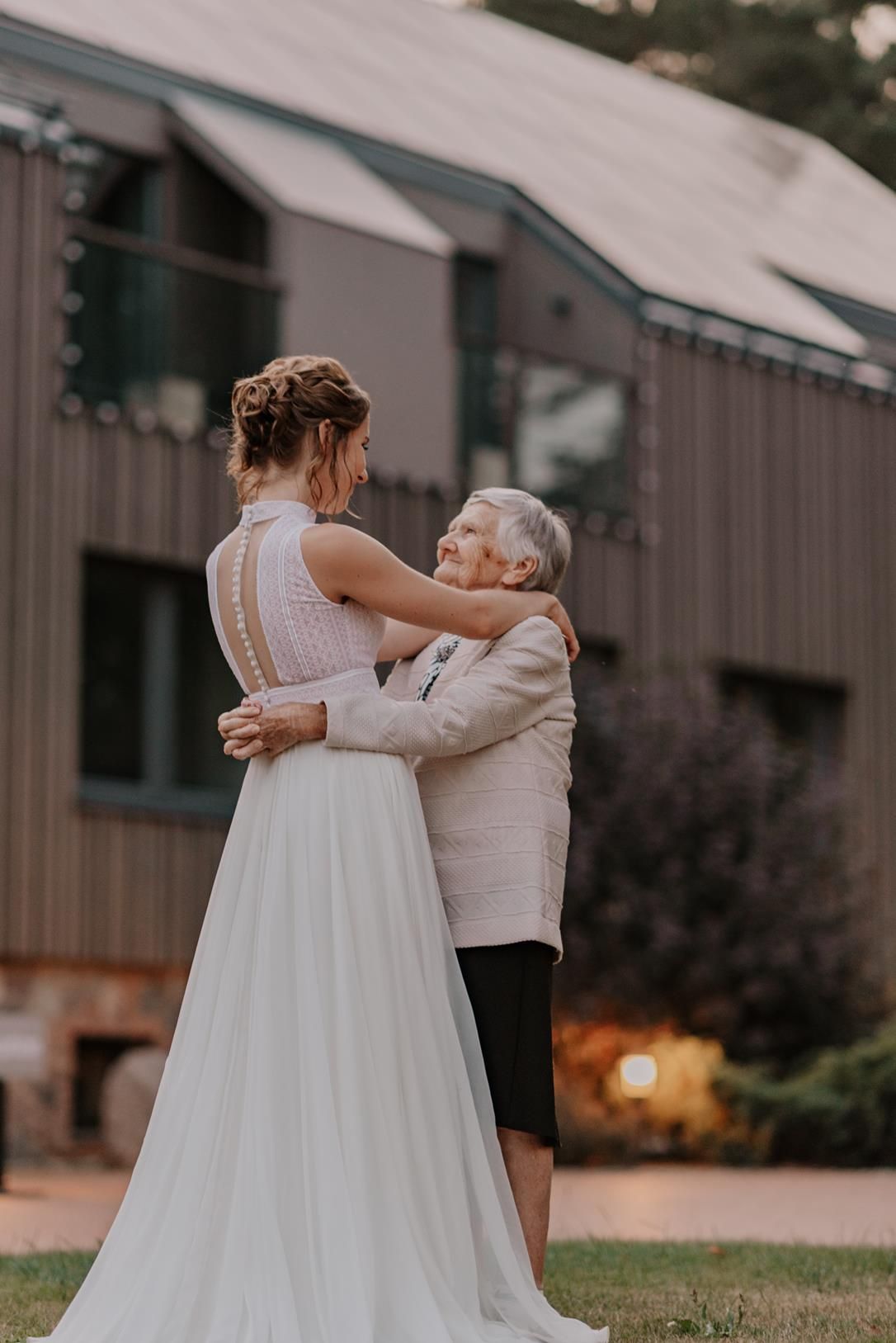 A touching embrace between a bride and elderly relative outside a rustic building.