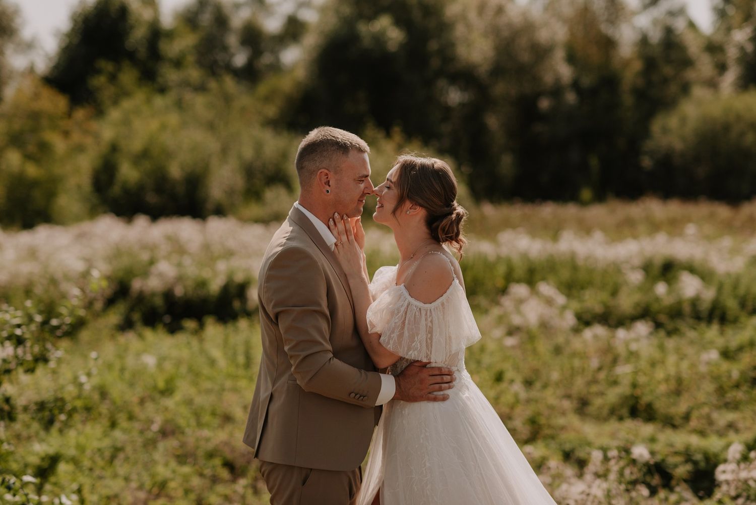 Newlywed couple embracing in a field of golden flowers during sunset.
