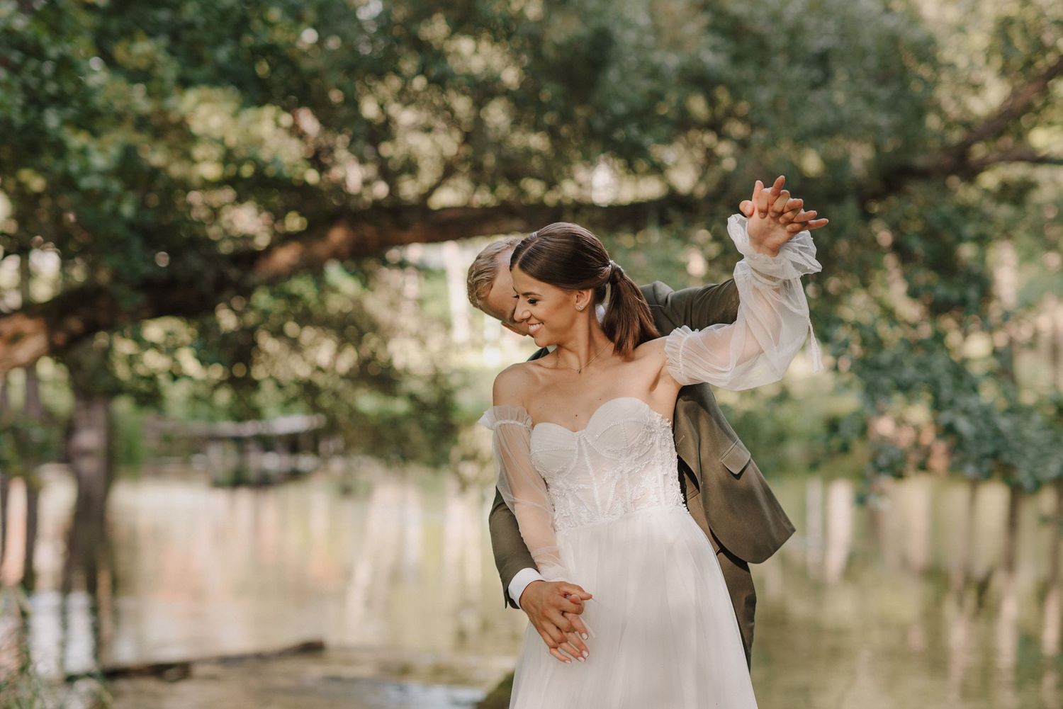 Wedding couple dancing playfully outdoors with natural scenery in background.