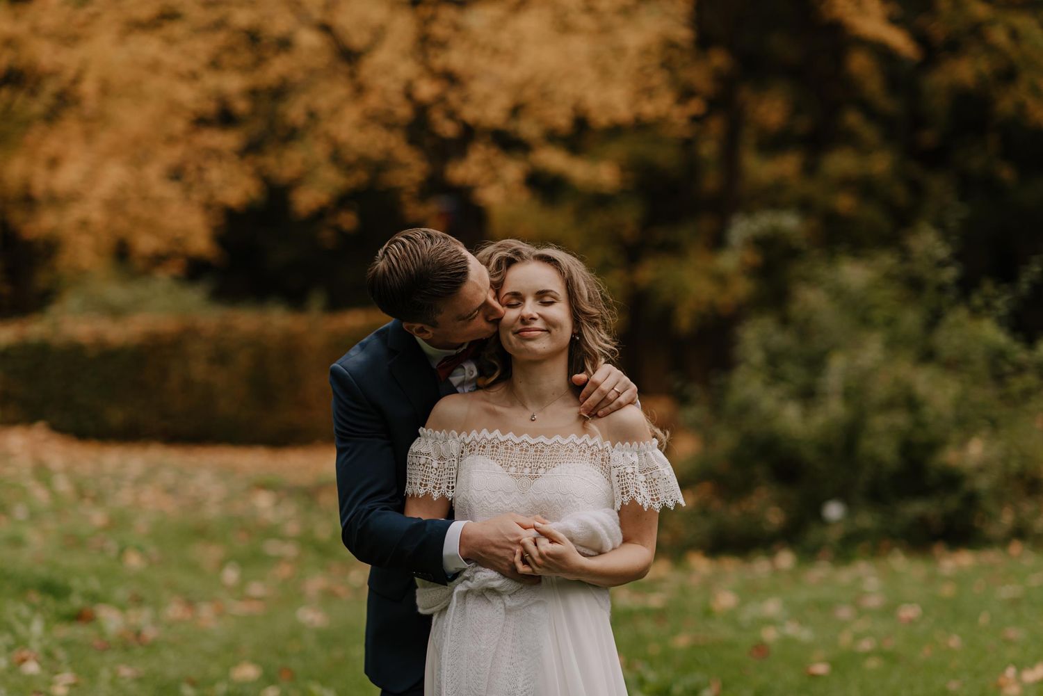 Romantic autumn wedding moment captured against warm orange and green foliage.