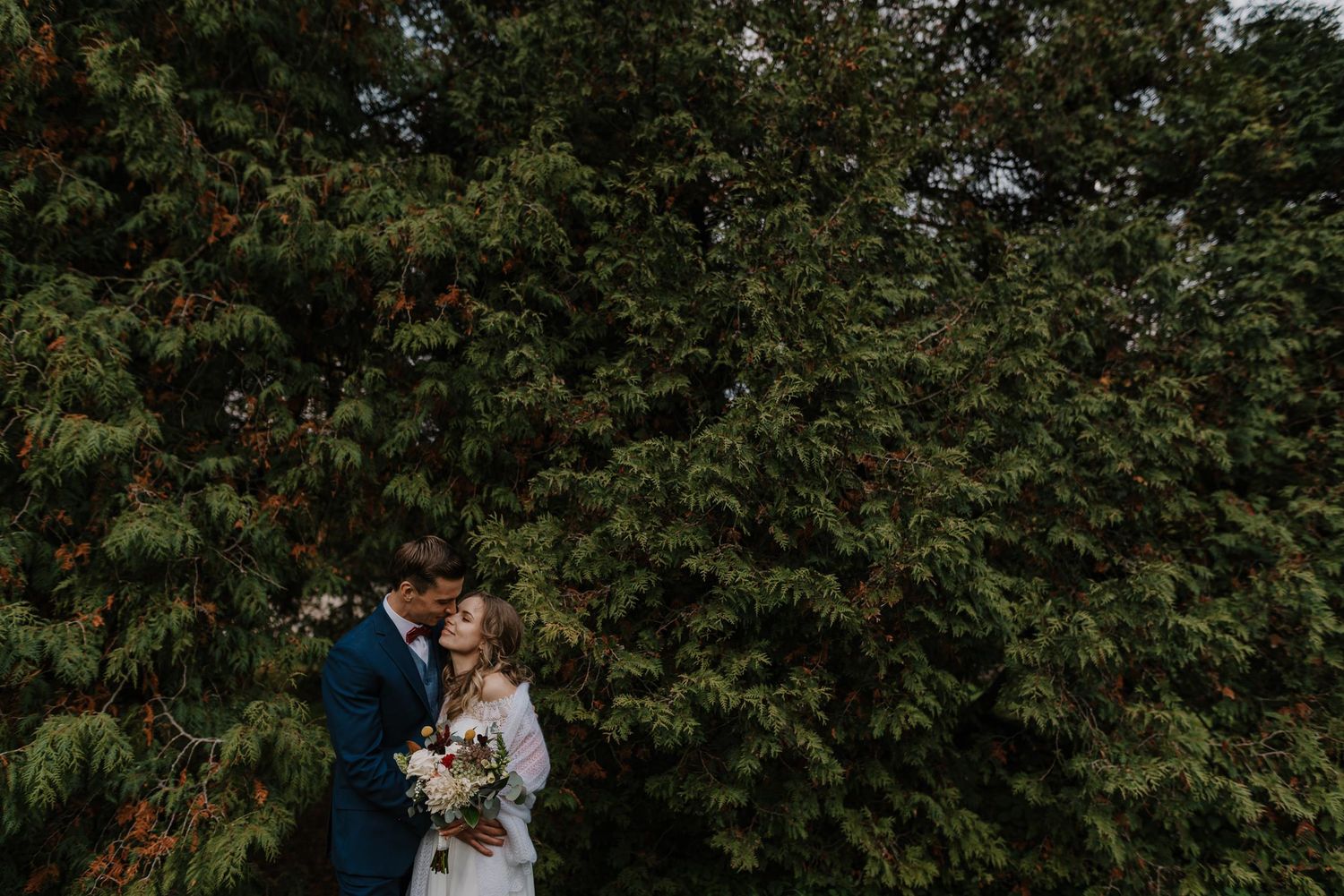 Intimate wedding moment captured among lush green trees and natural scenery.