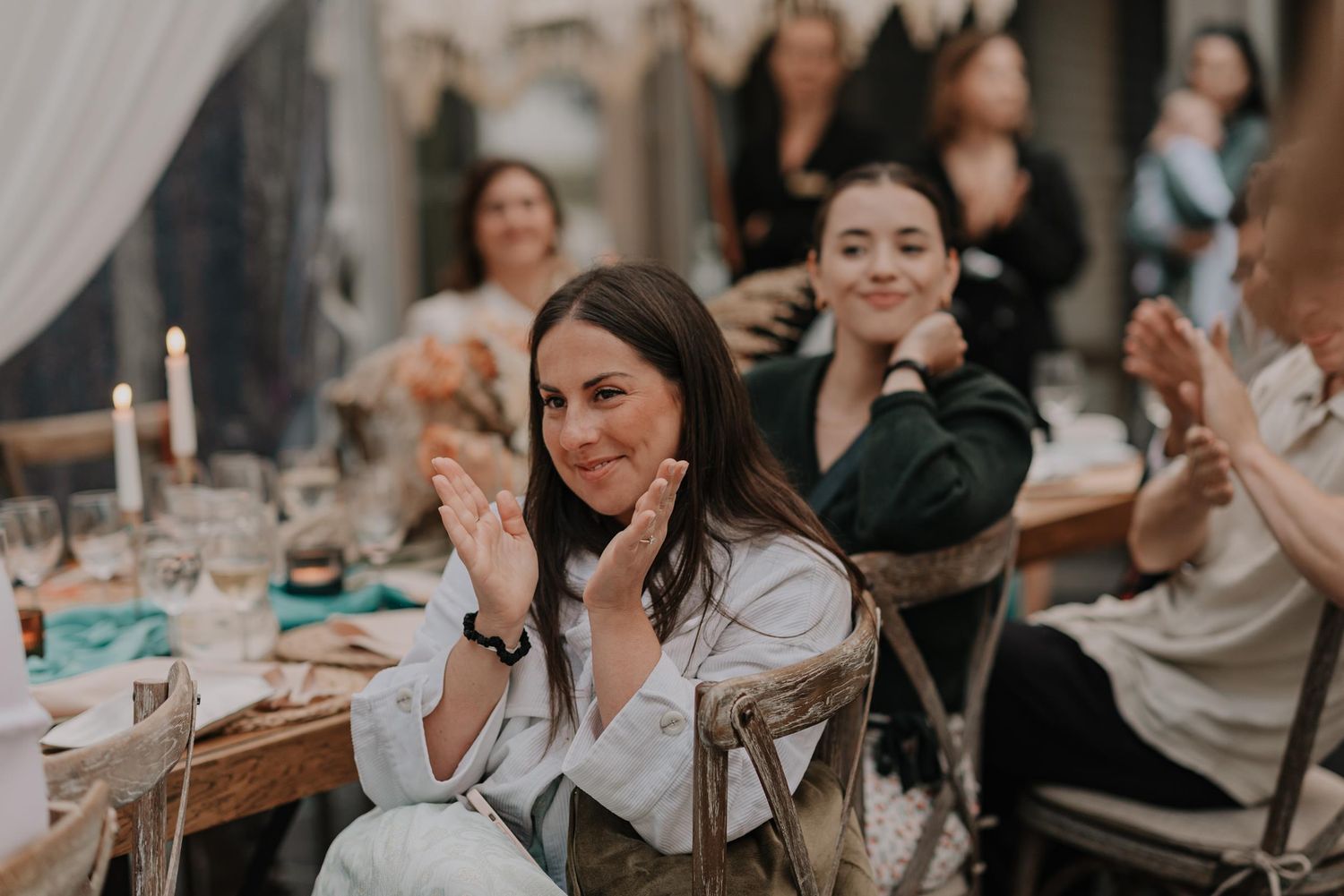 Wedding reception guests seated at tables smile and laugh during dinner.