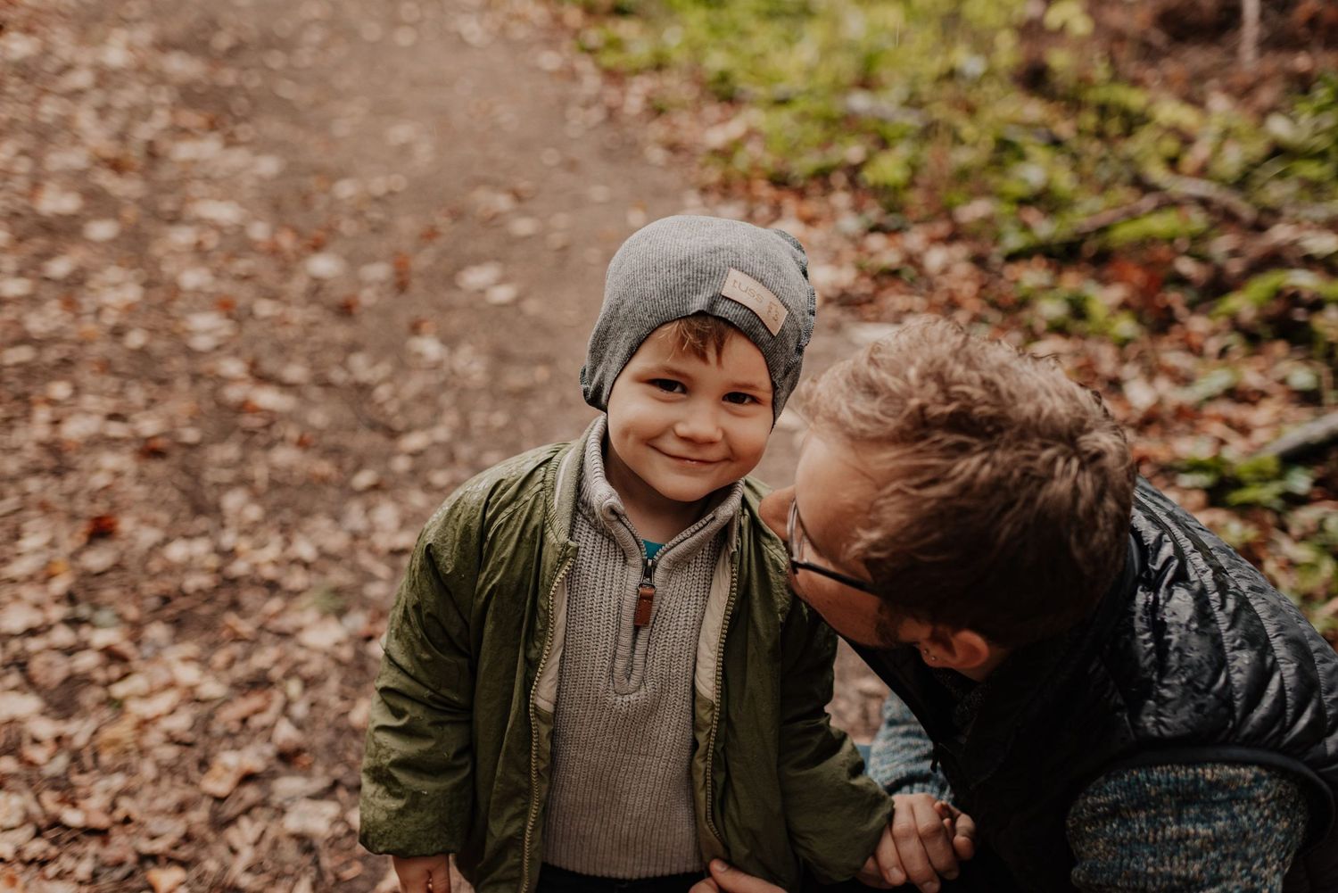 Parent and child share a tender moment while playing in autumn leaves on a forest trail.