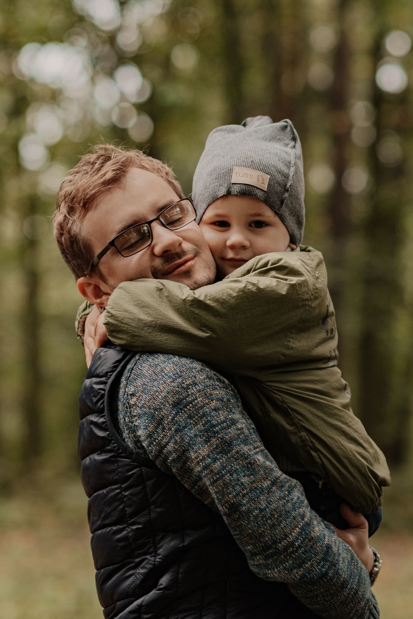 A couple embraces in a forest setting with autumn bokeh lights in the background.