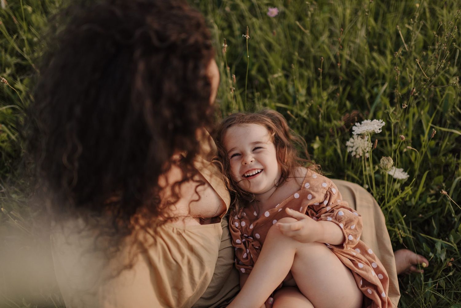 Two people share a joyful moment laying in a sunny wildflower meadow.