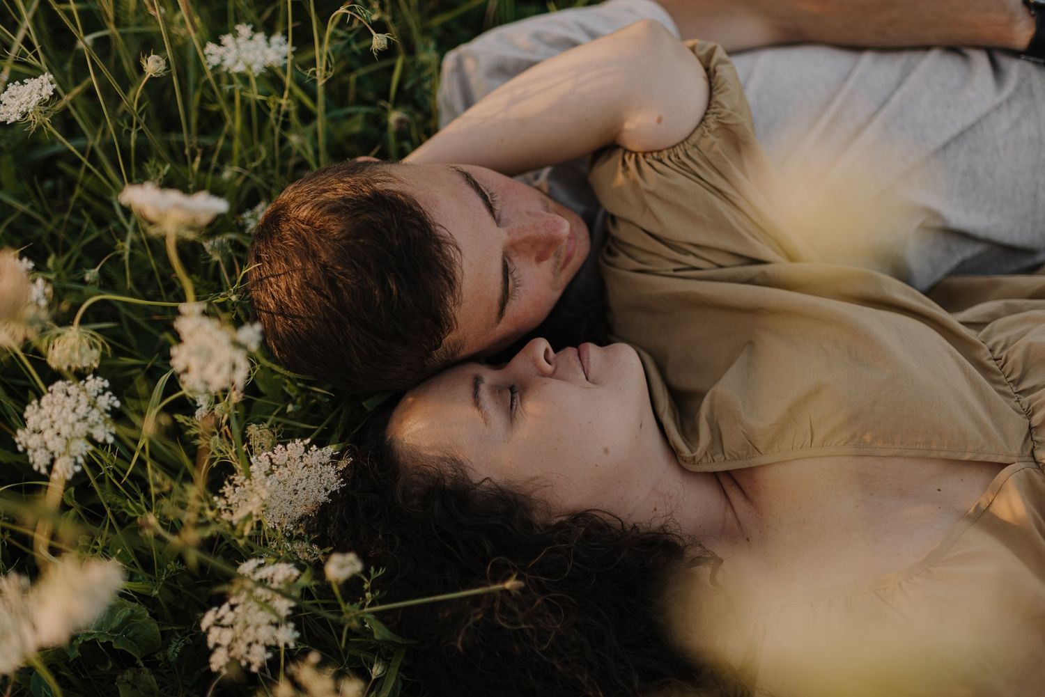Two people lying peacefully in a meadow surrounded by white wildflowers.
