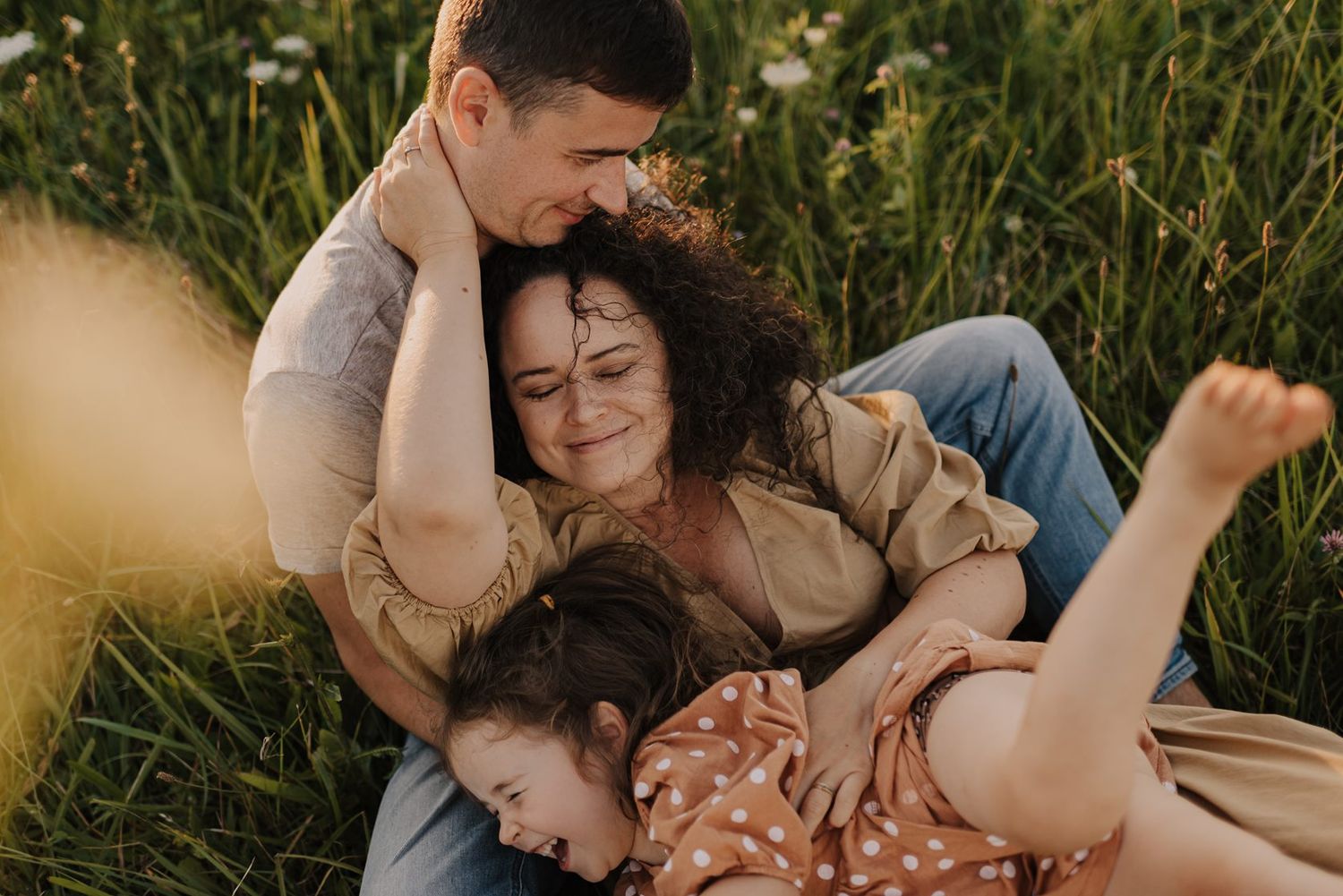 Family embracing together in a summer meadow filled with wildflowers.