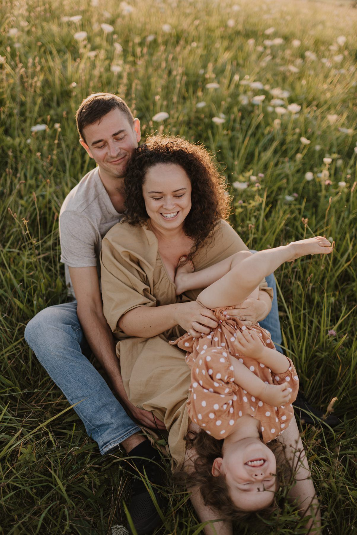 Playful family moment captured in tall grass during golden hour.
