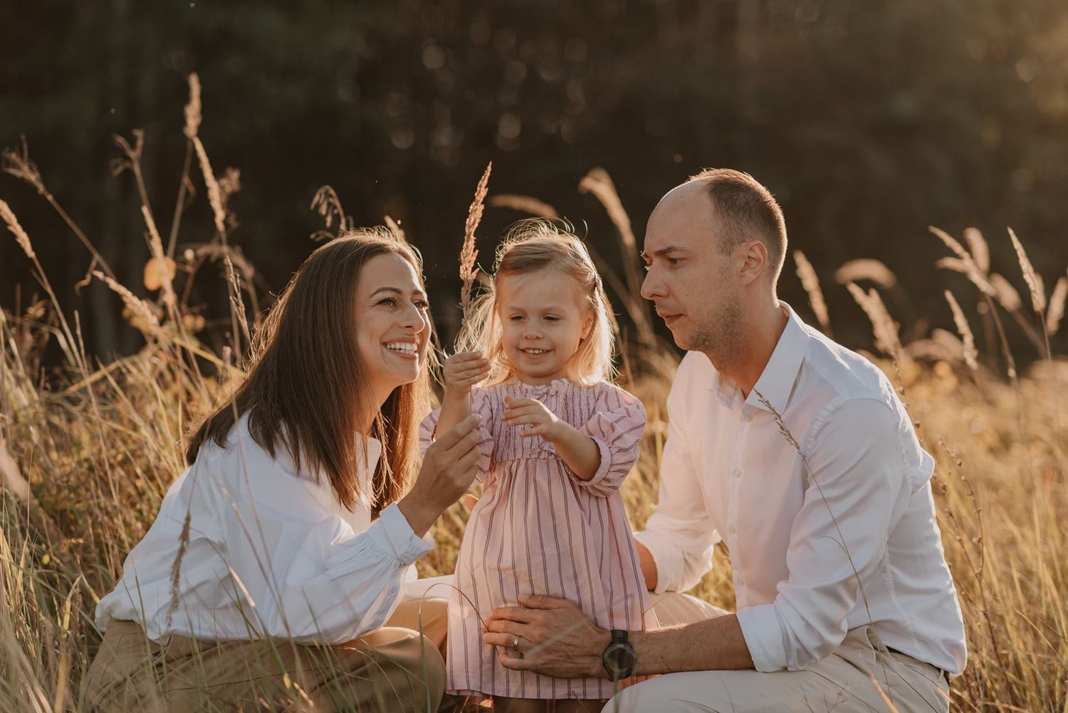 Family shares joyful moments together in a golden wheat field at dusk.