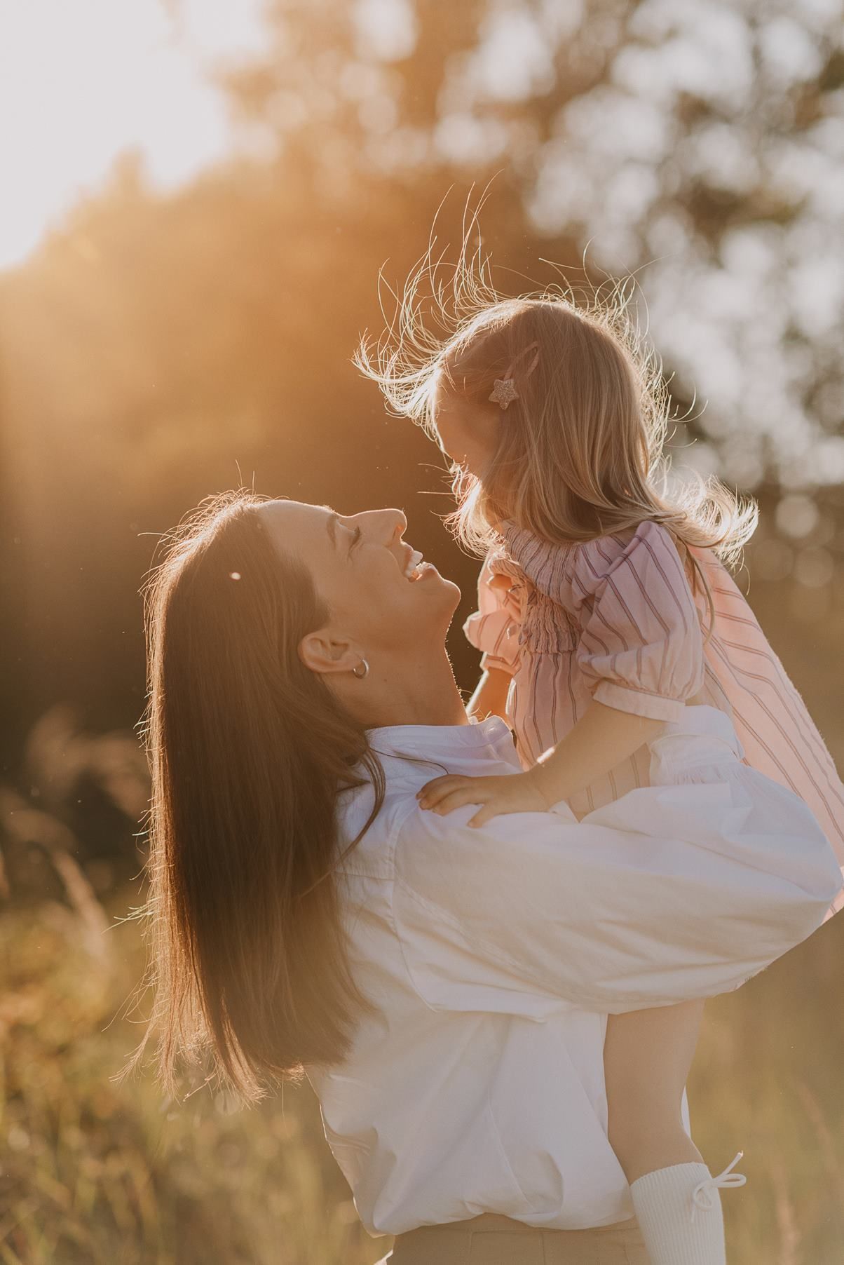 Family embraces and plays together in warm evening sunlight.