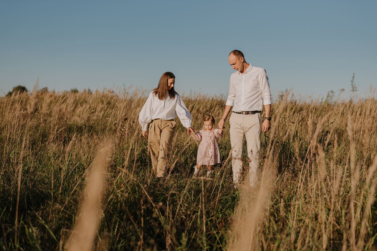 Family walks through tall grass field during sunset photoshoot.