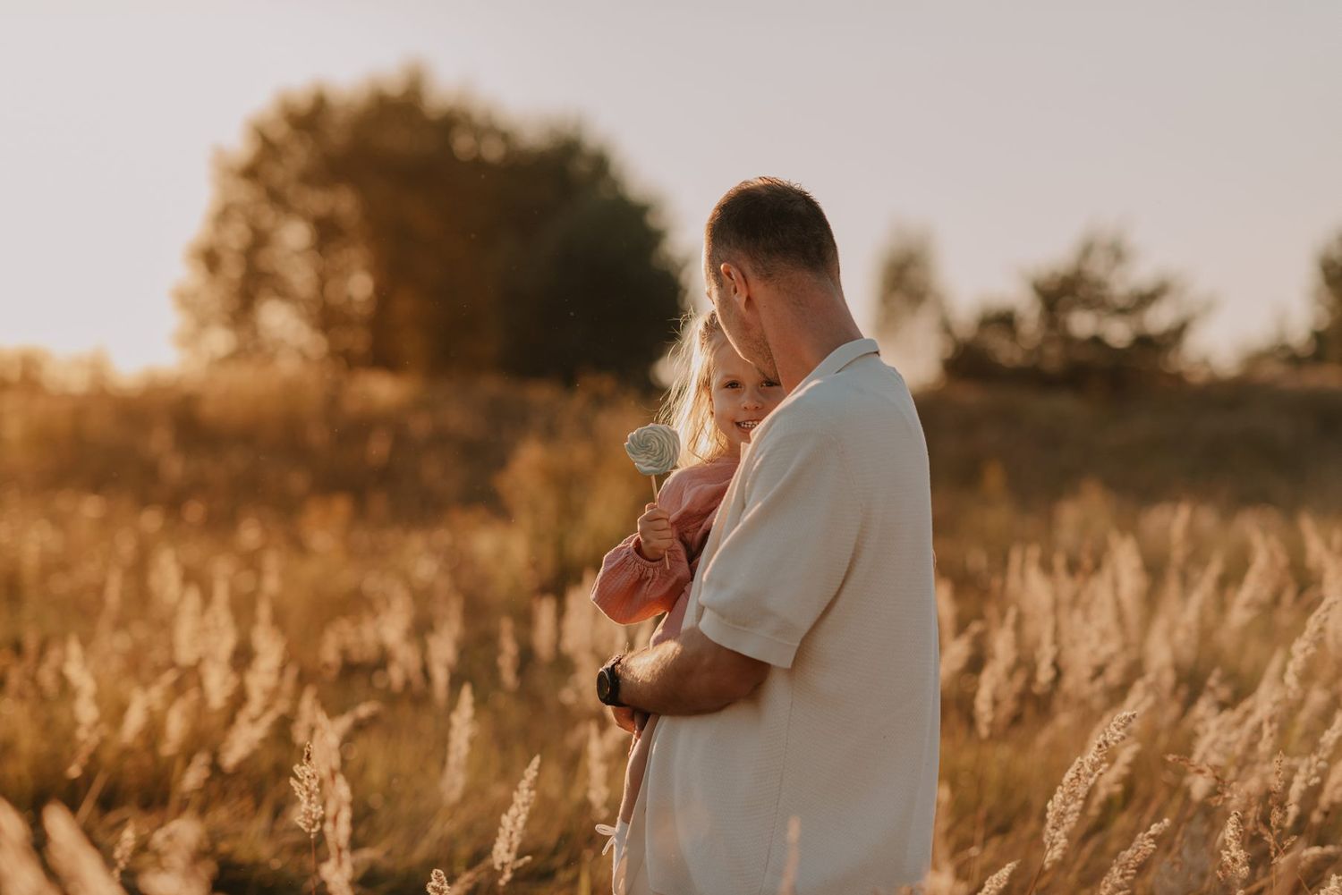 Family outdoor photoshoot in a field of tall grass during golden hour sunset.