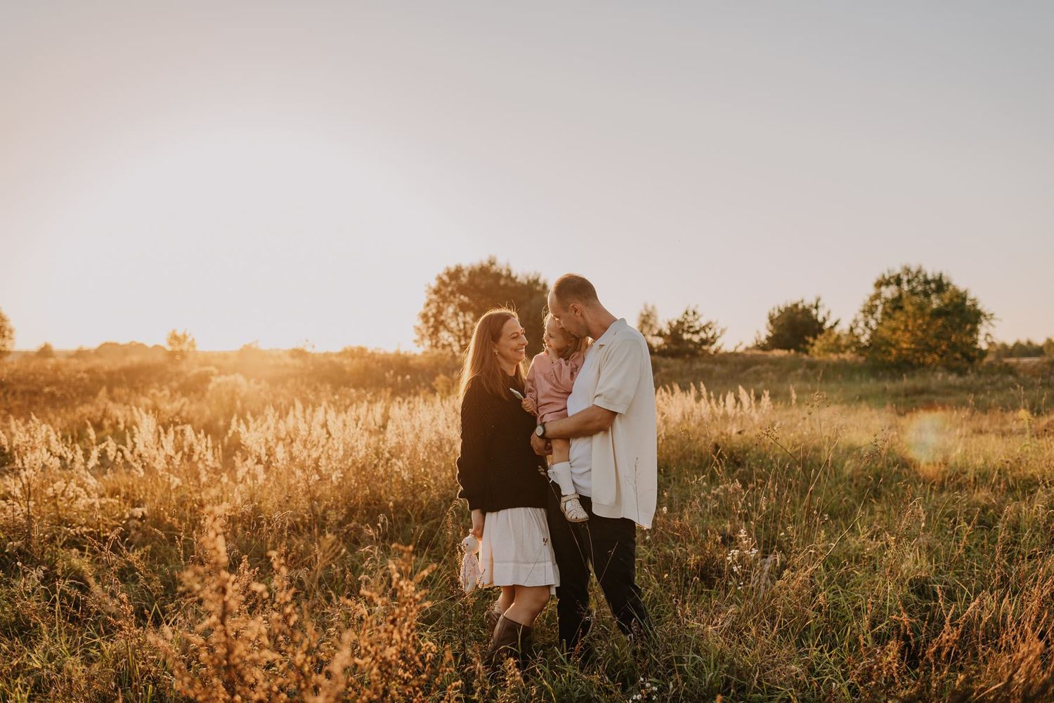 Tender family moments photographed in a meadow with soft sunlight filtering through.