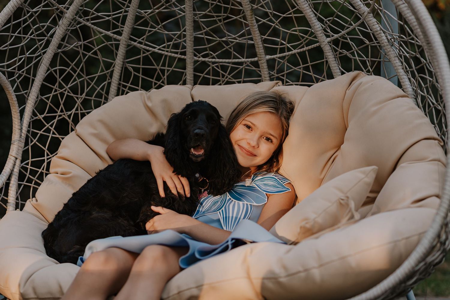 Cozy family cuddles in a hanging wicker egg chair outdoors.