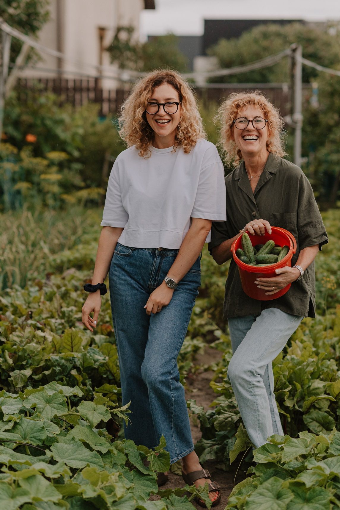 Two people laugh together while harvesting vegetables from their garden.