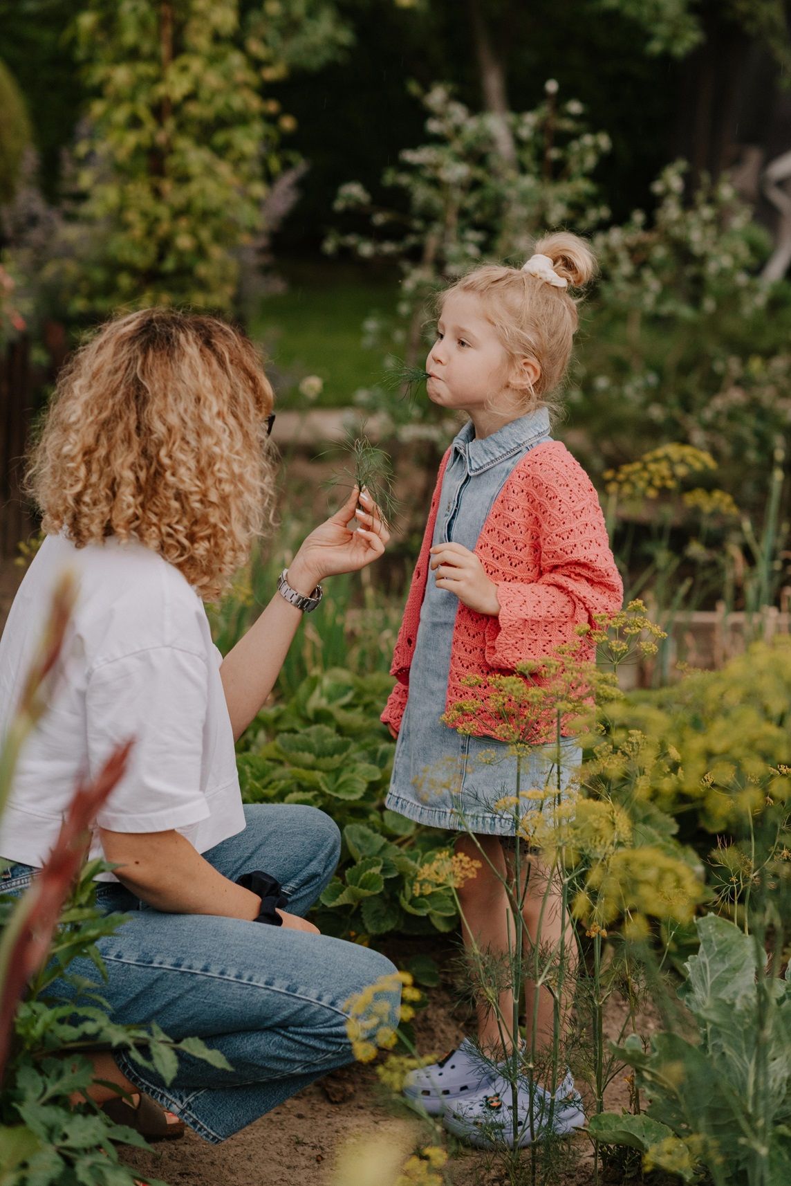 Two people sit together in a flourishing garden discussing plants and vegetables.
