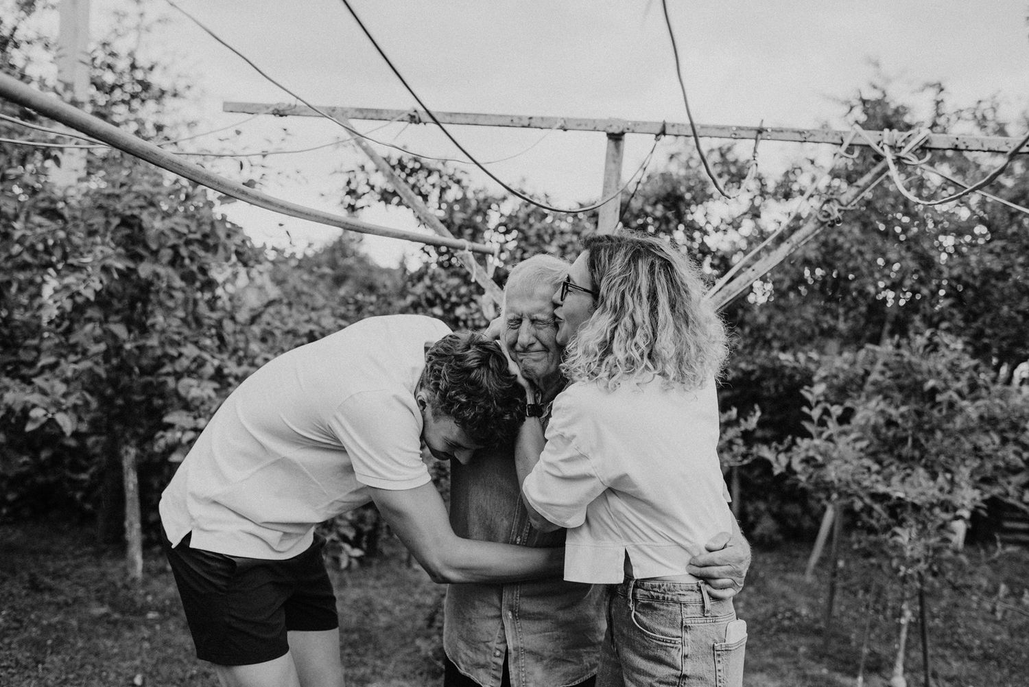 A loving couple embraces in a yard with trees and power lines visible in the background.