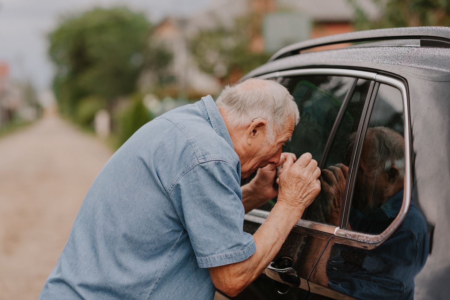 A person in blue clothing peers into a car window on a sunny day.
