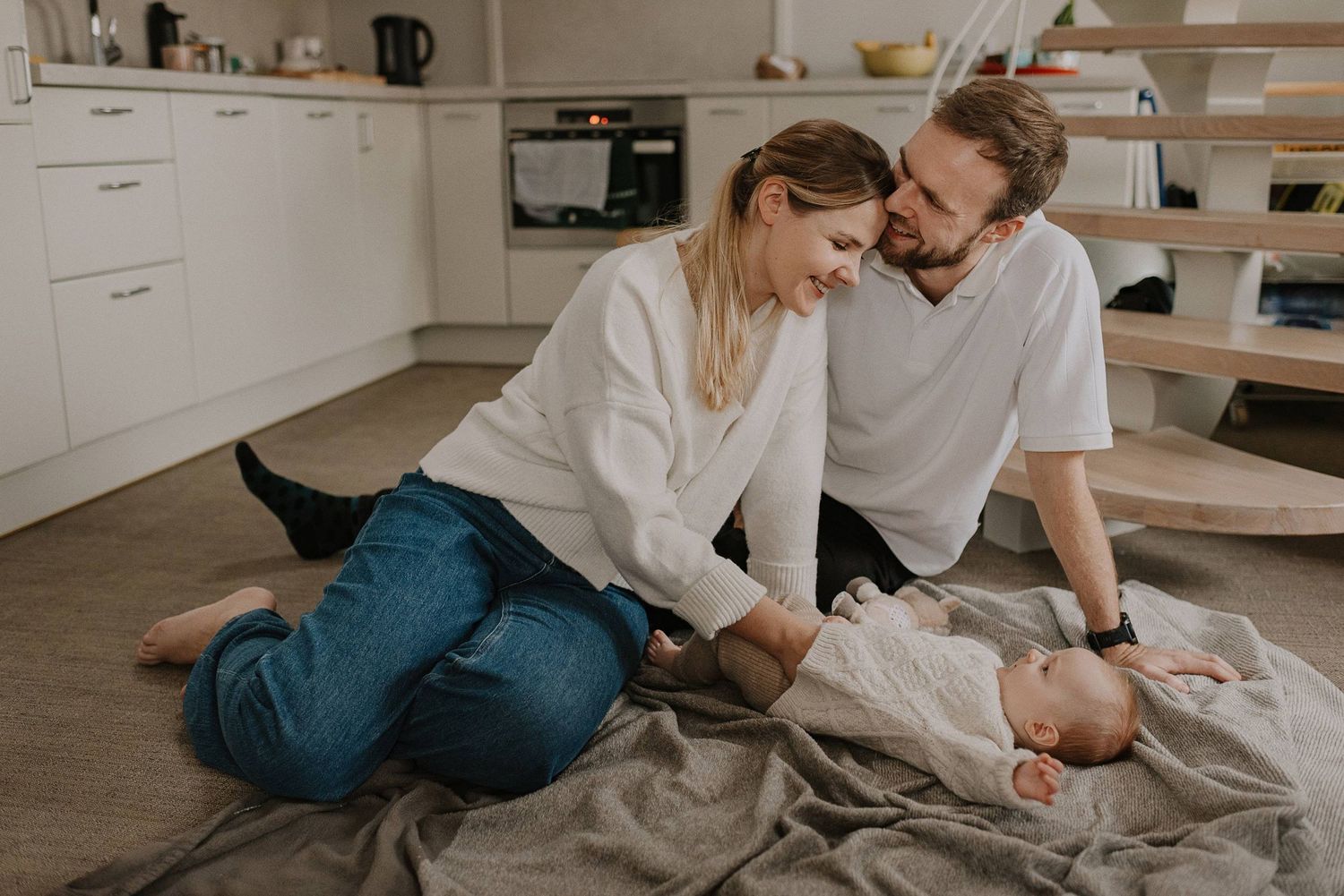 Parents spending quality time with baby on floor of modern kitchen.