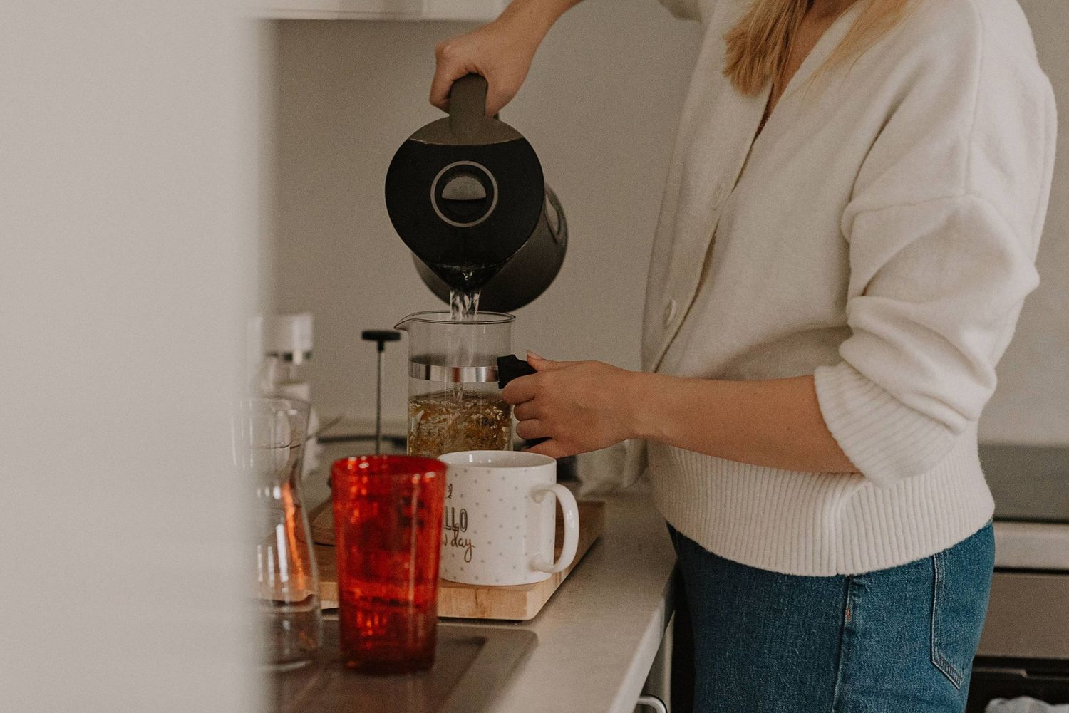 Person pouring from black kettle into coffee maker in kitchen setting.