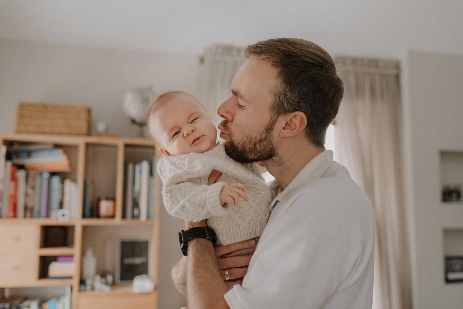 Sweet bonding moment with baby wearing knit sweater in bright home interior.