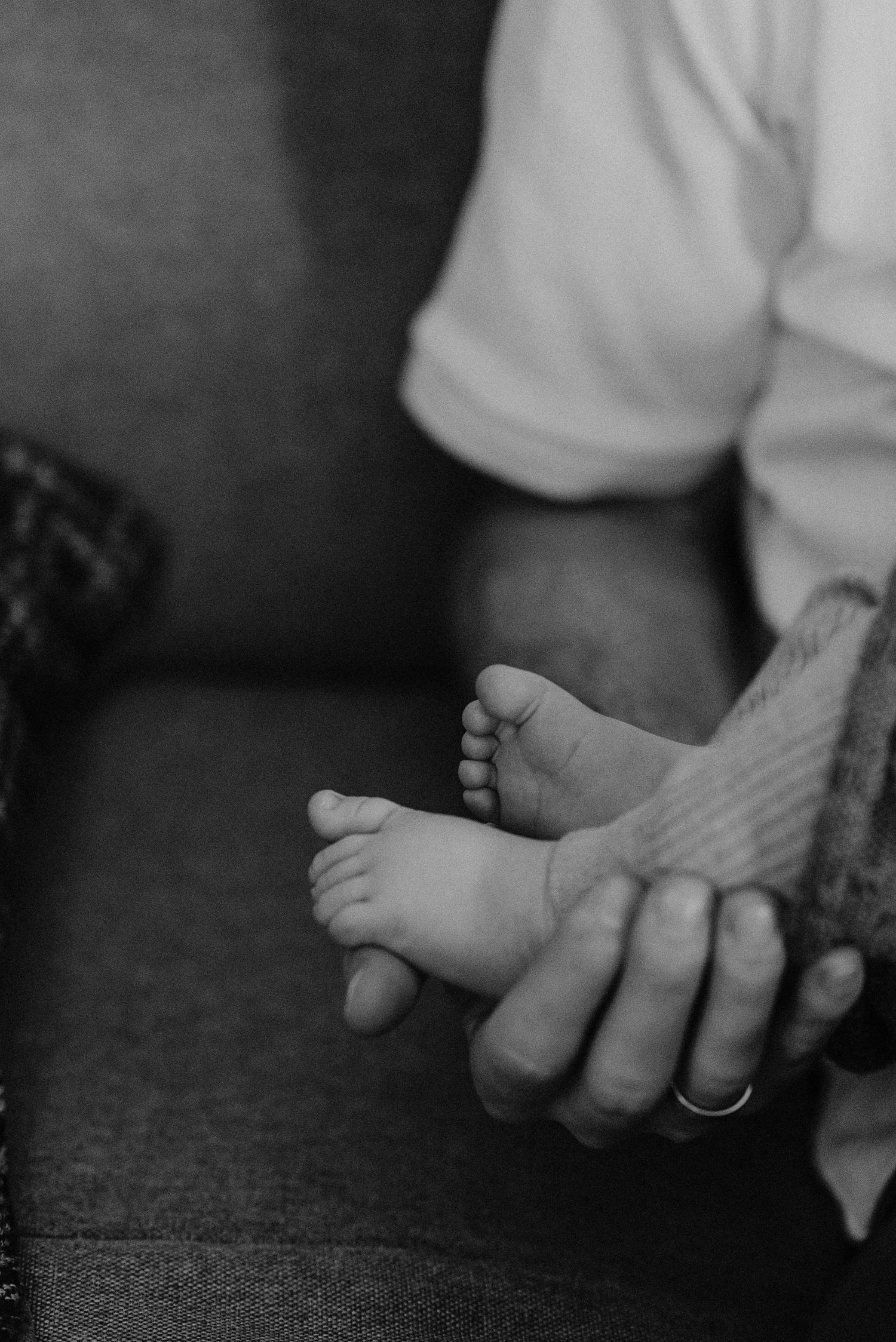 Close-up of tiny baby feet being held by gentle hands on dark fabric.
