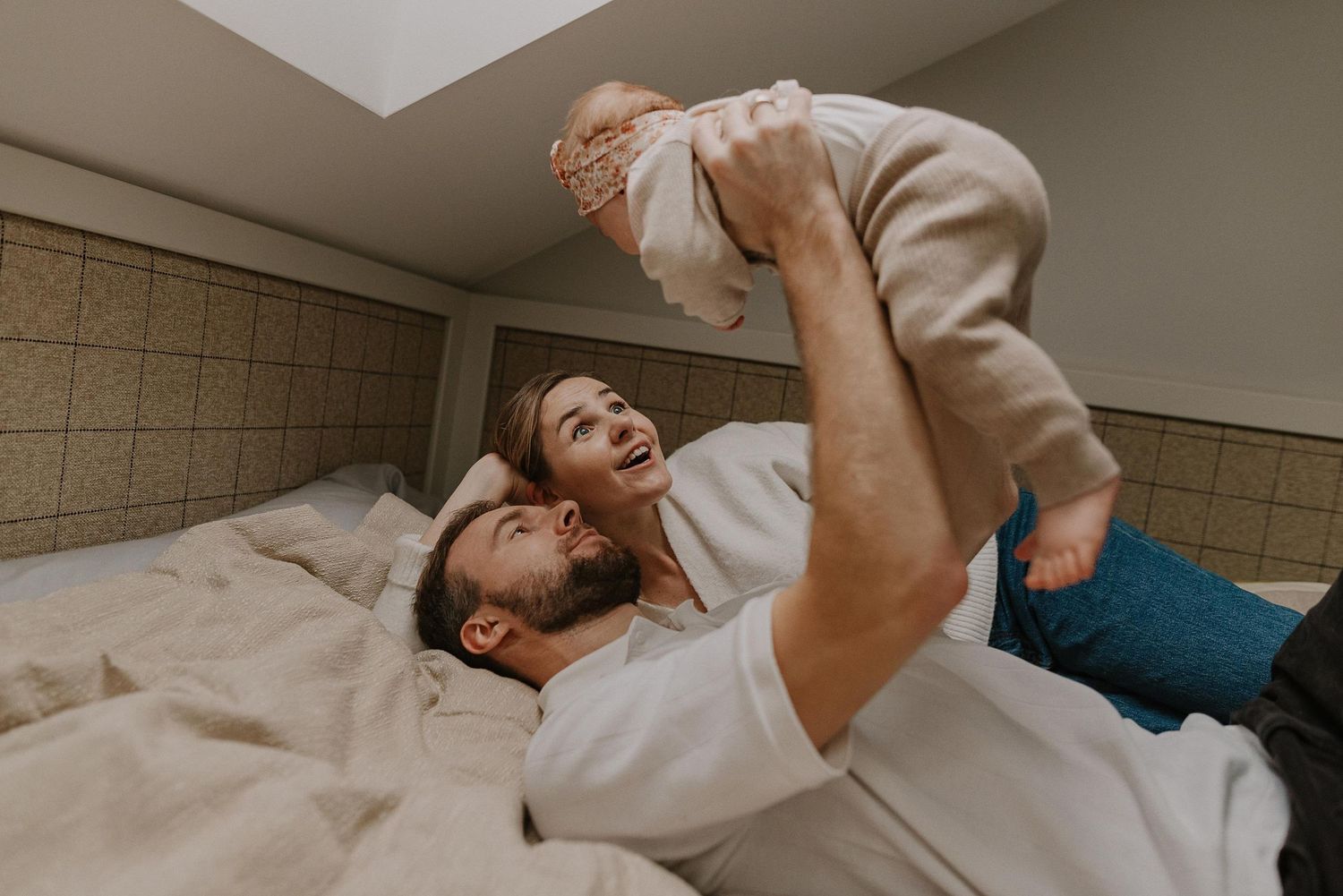 Joyful playtime moment with baby being lifted up on comfortable bed.