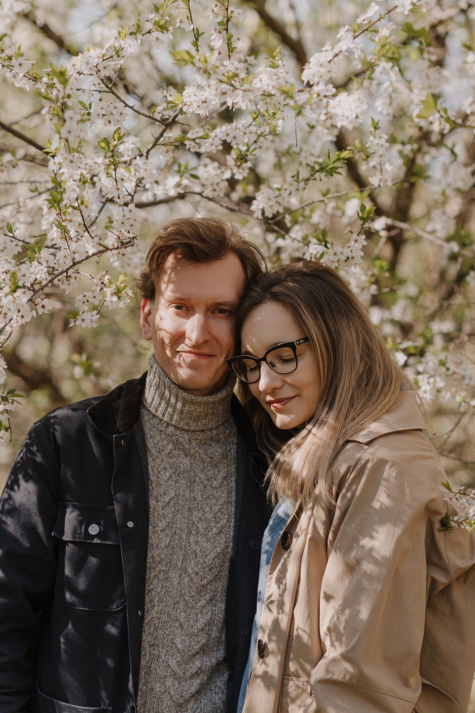 Romantic couple portrait beneath blooming cherry blossoms in spring.
