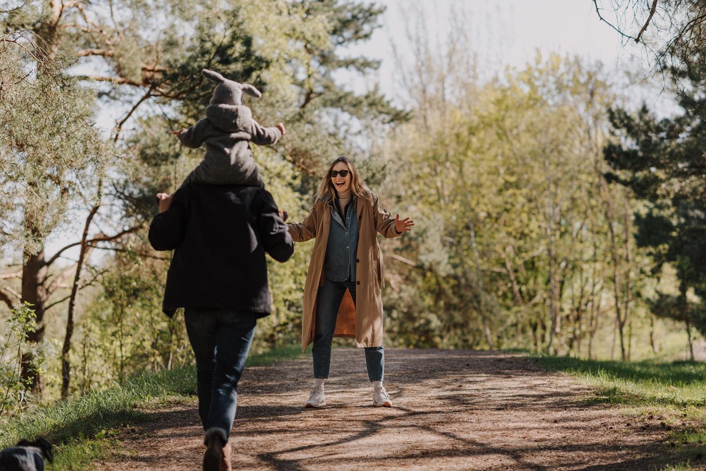 People strolling down a wooded path on a sunny fall day with trees casting dappled shadows.