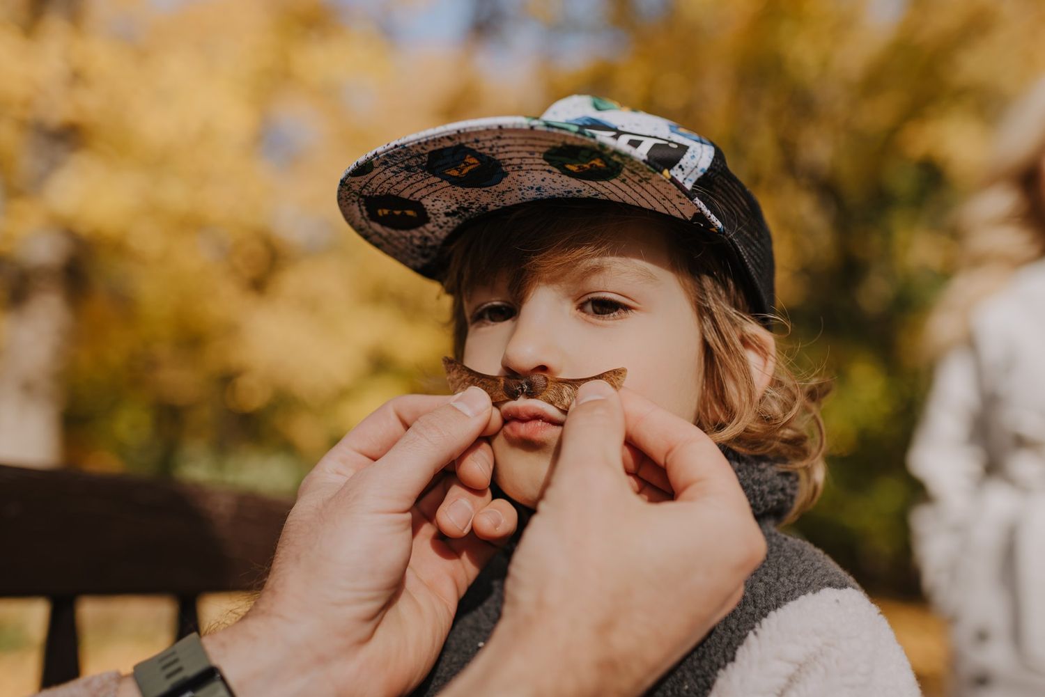 A family shares playful moments together picking berries from a bush in a sun-dappled outdoor setting.