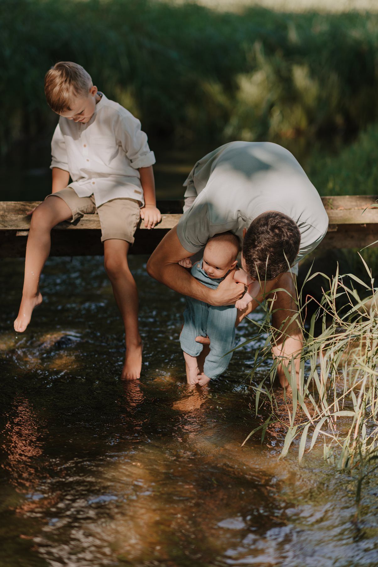 Serene moment at the creek's edge with feet dangling in crystal clear water among tall reeds and grass.
