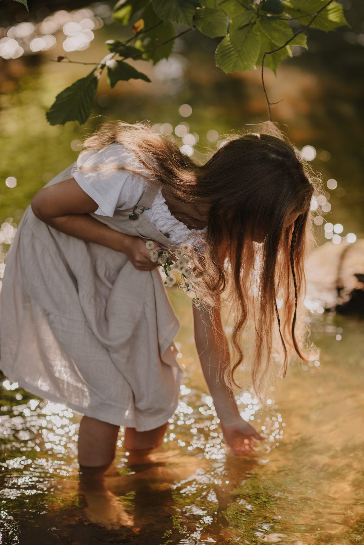 Dreamy afternoon light illuminates children playing in shallow creek water wearing light-colored outfits.