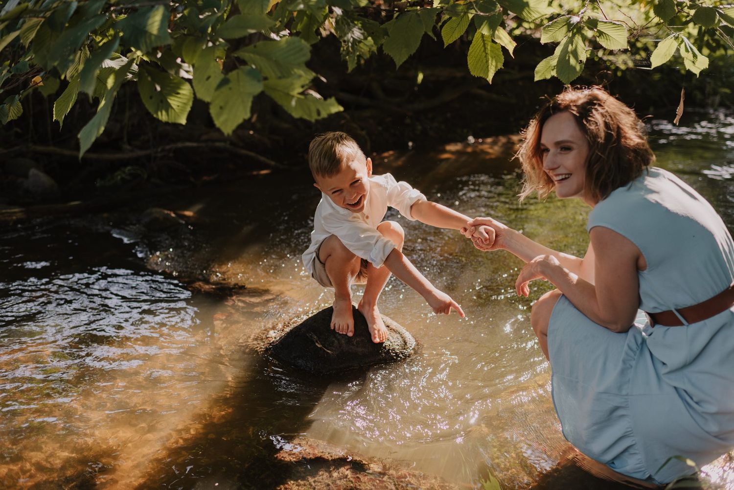 People in light blue and white outfits playing and splashing in a sun-dappled stream.