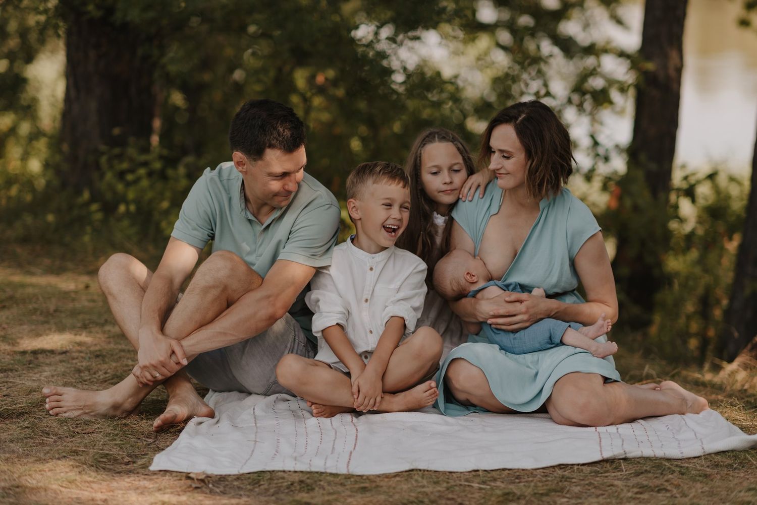 Family relaxing together on a white blanket during an outdoor photo session.
