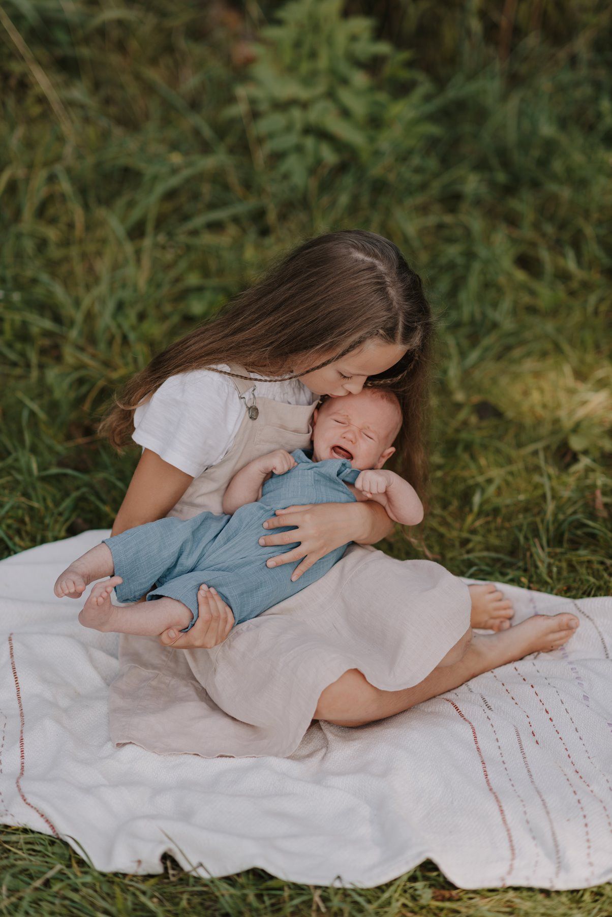 Sweet family cuddles on a white blanket in a grassy outdoor setting.