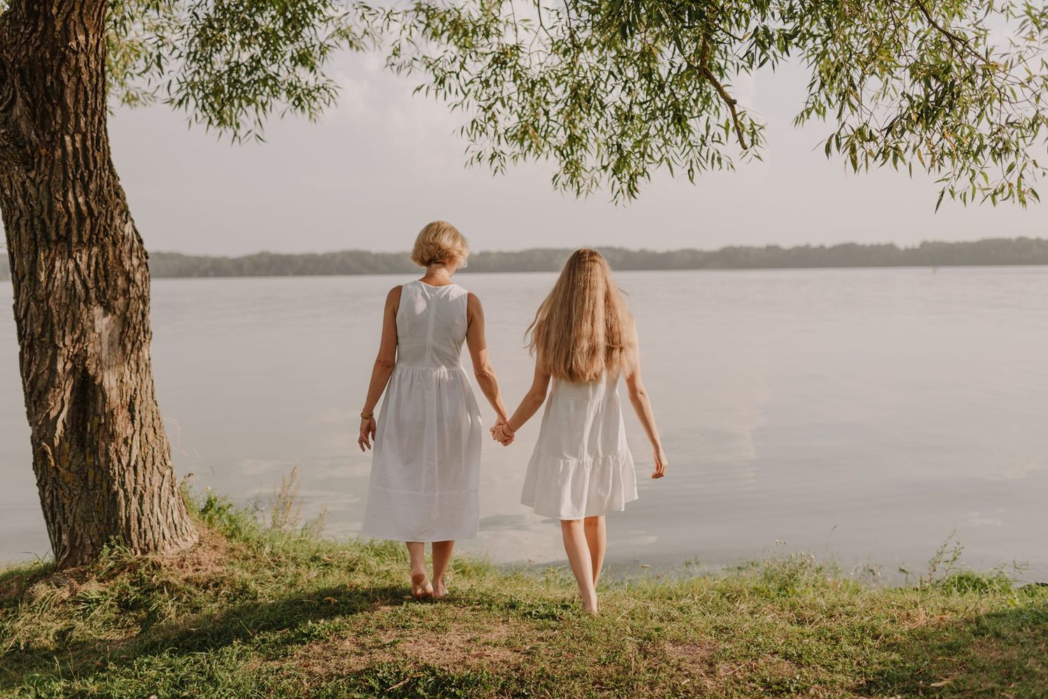 People stand by a tranquil lake under weeping willow trees on a peaceful afternoon.