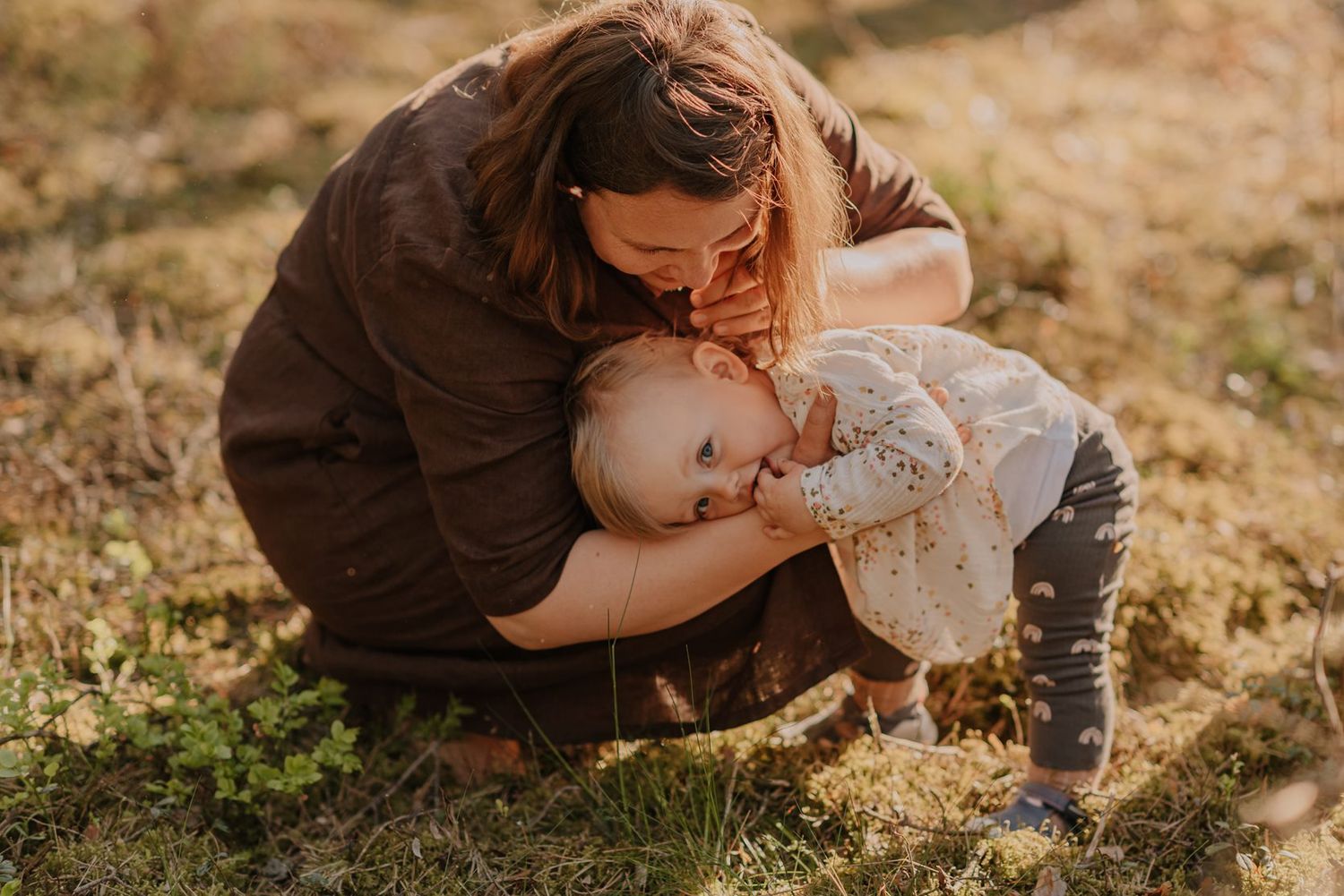 Parent and child share playful moments together on grassy ground during a sunny afternoon.