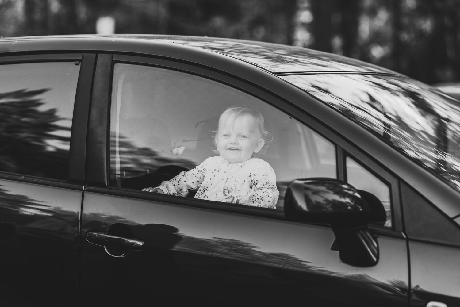 A black and white image of a small child looking through a car window with a joyful expression.