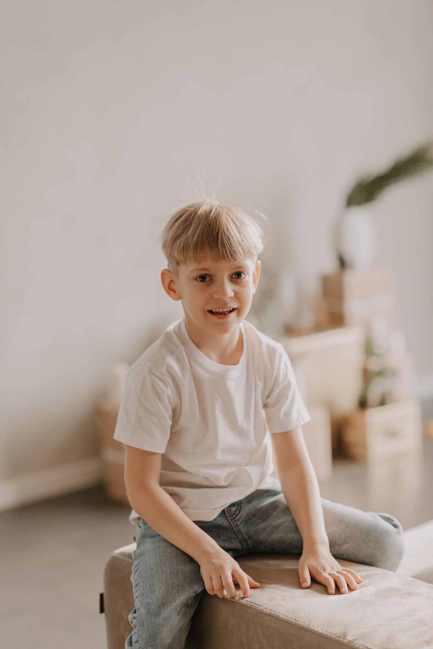 A young child in a white t-shirt sitting casually on a light-colored couch.