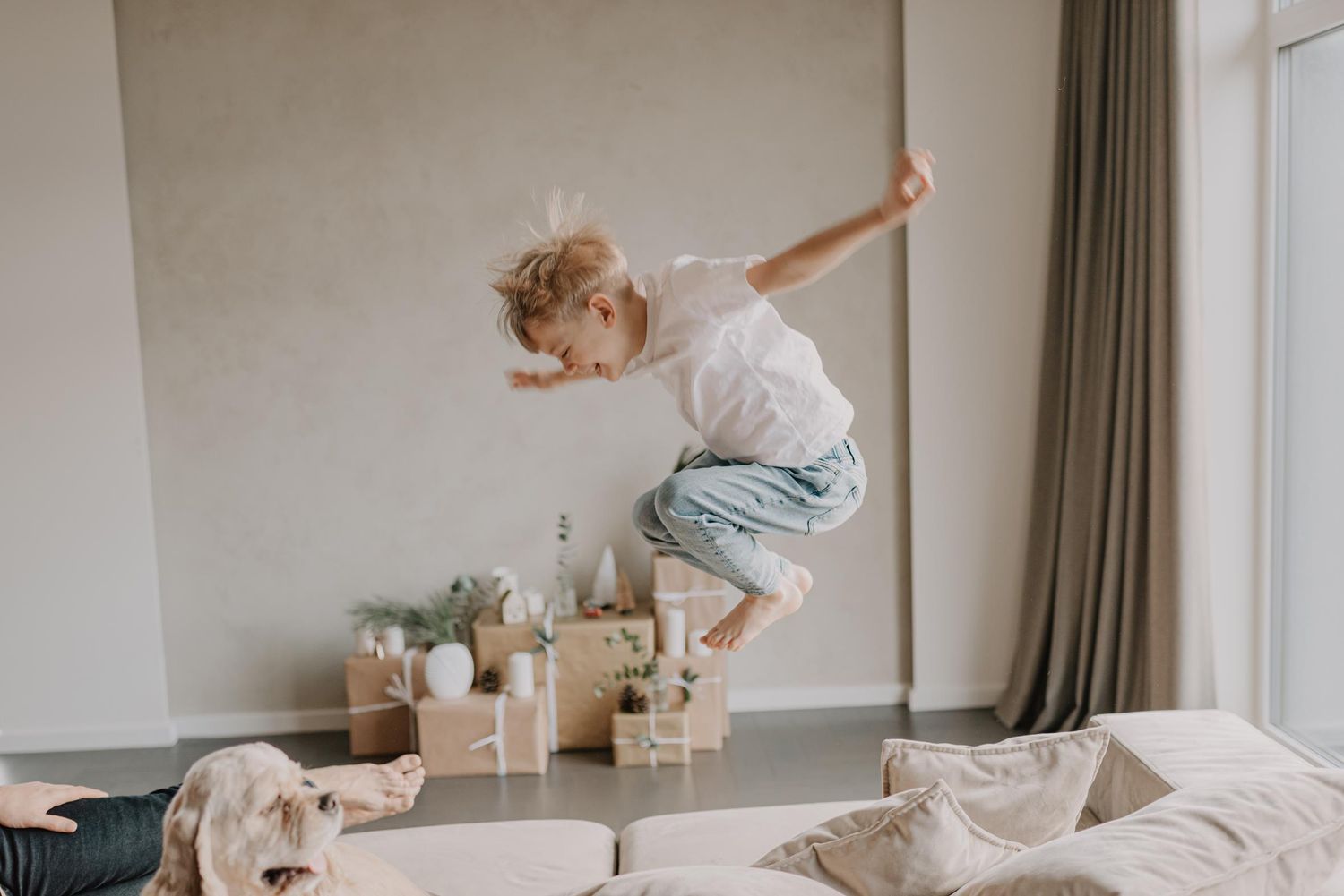 Energetic child jumping high above wooden blocks while a dog watches nearby.