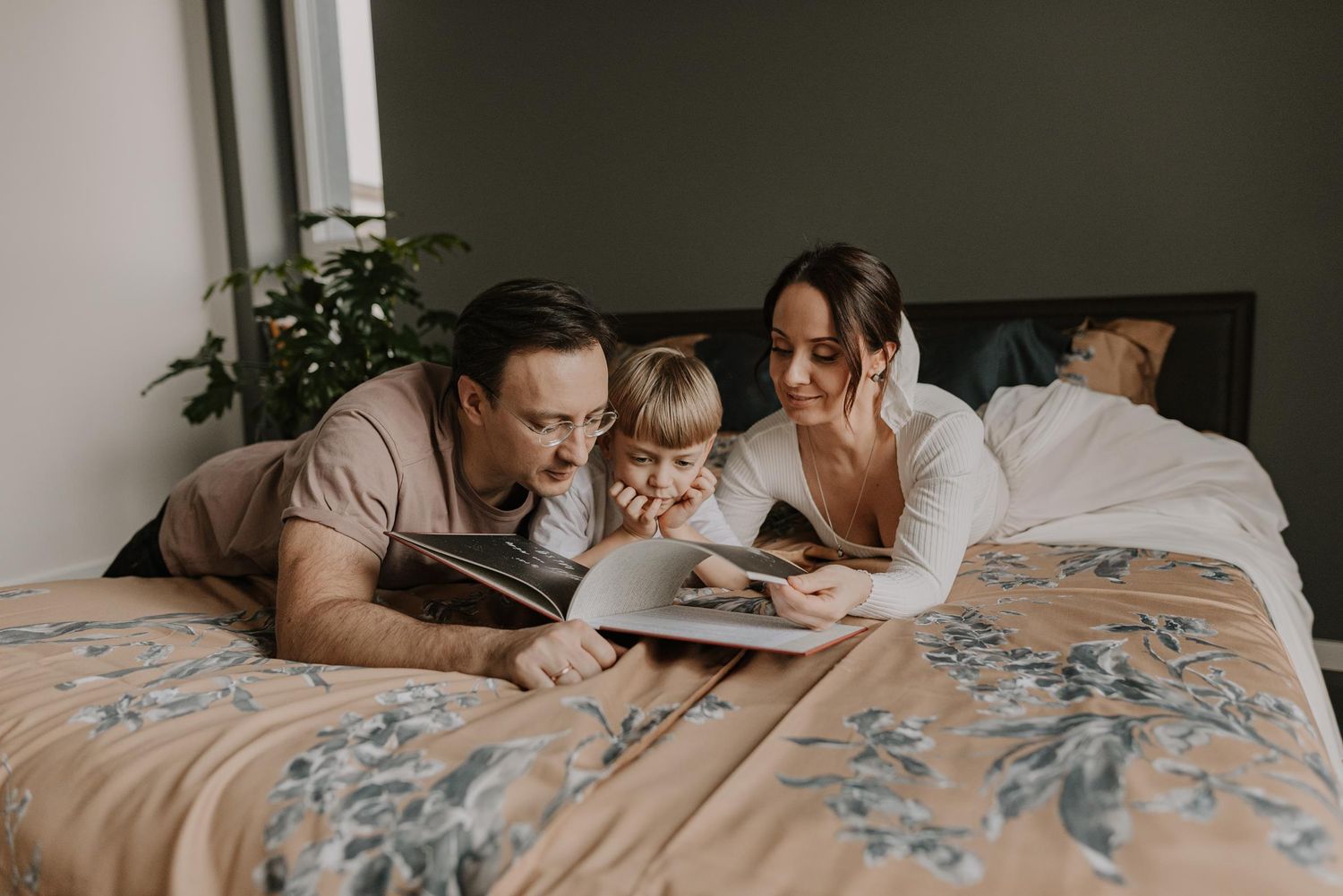 Family relaxing together on floral patterned bedding in natural light.