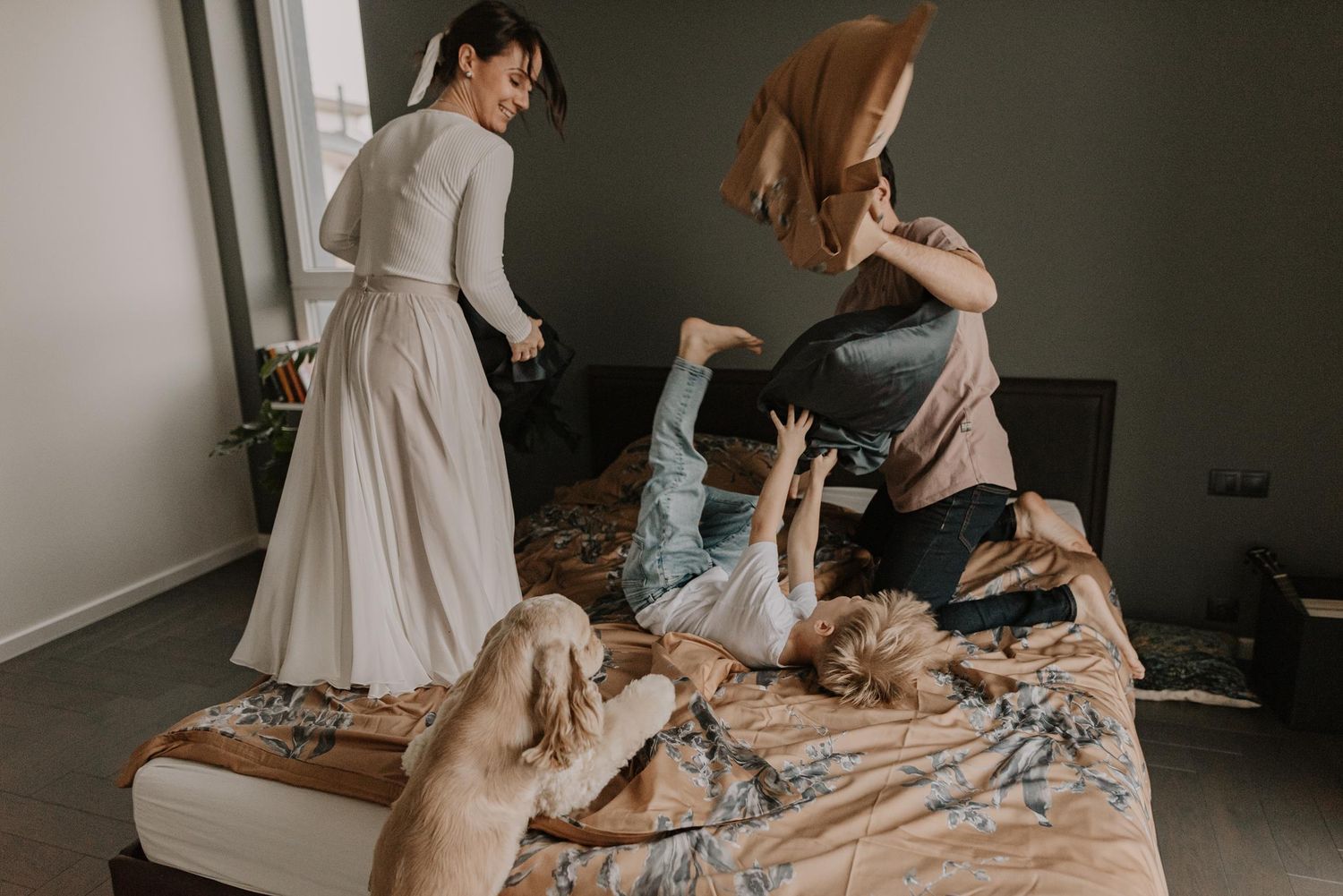 Joyful family pillow fight on bed with natural window lighting.