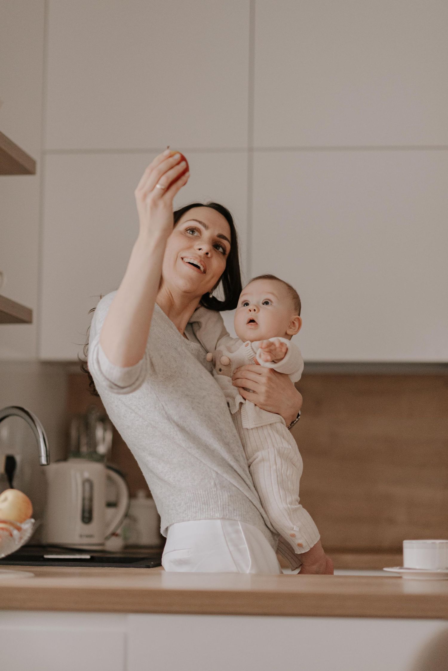 Parent and baby share playful mealtime moment in bright modern kitchen.