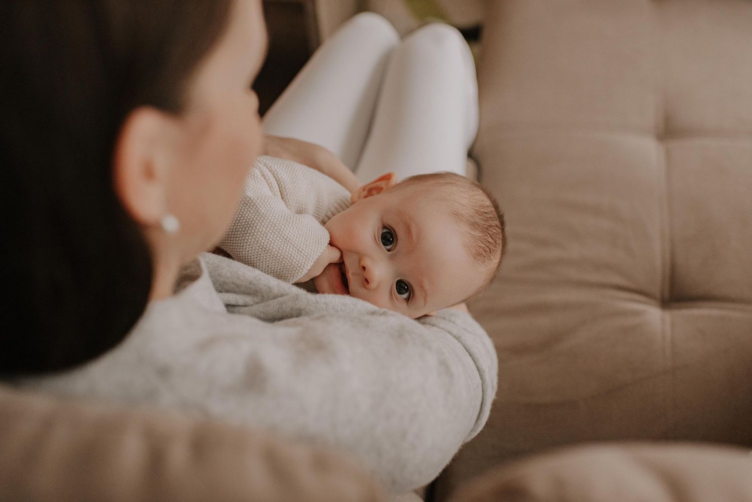 Baby lying on couch making eye contact with parent in cozy indoor setting.