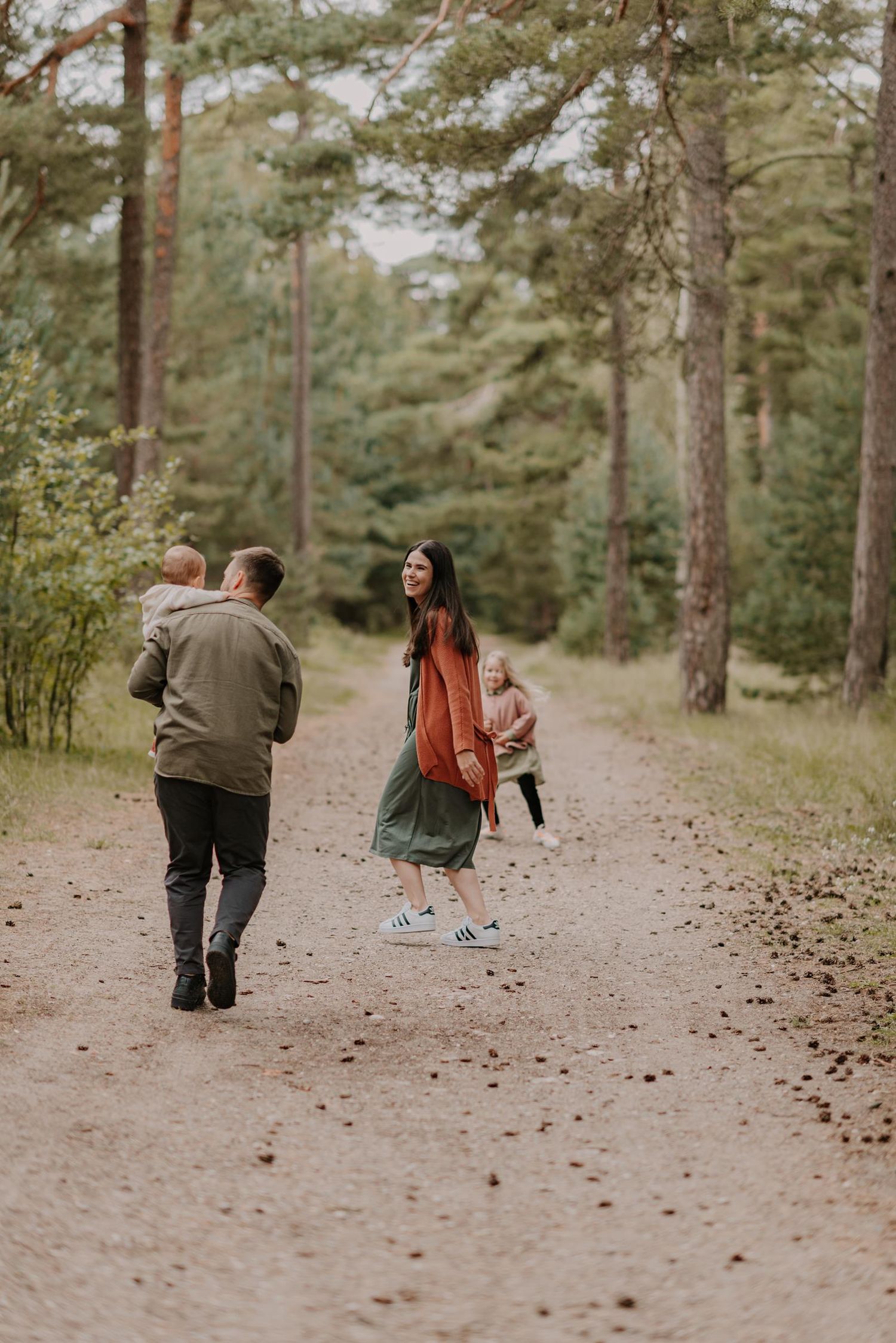 Family walking together on a winding path through a pine forest.