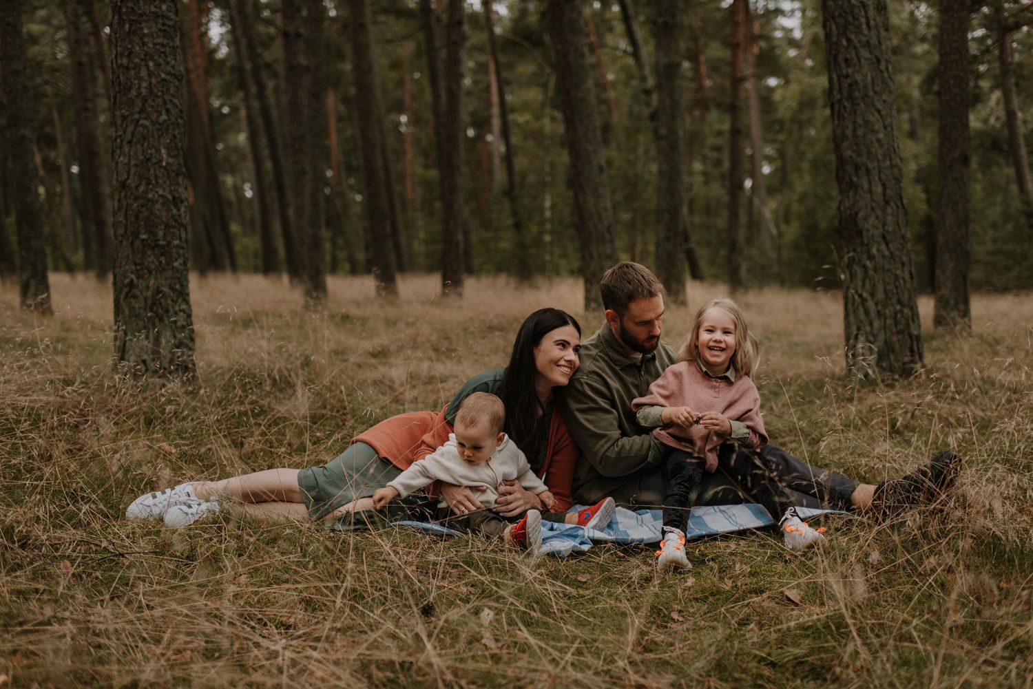 Family enjoying quality time together on blanket in pine forest.