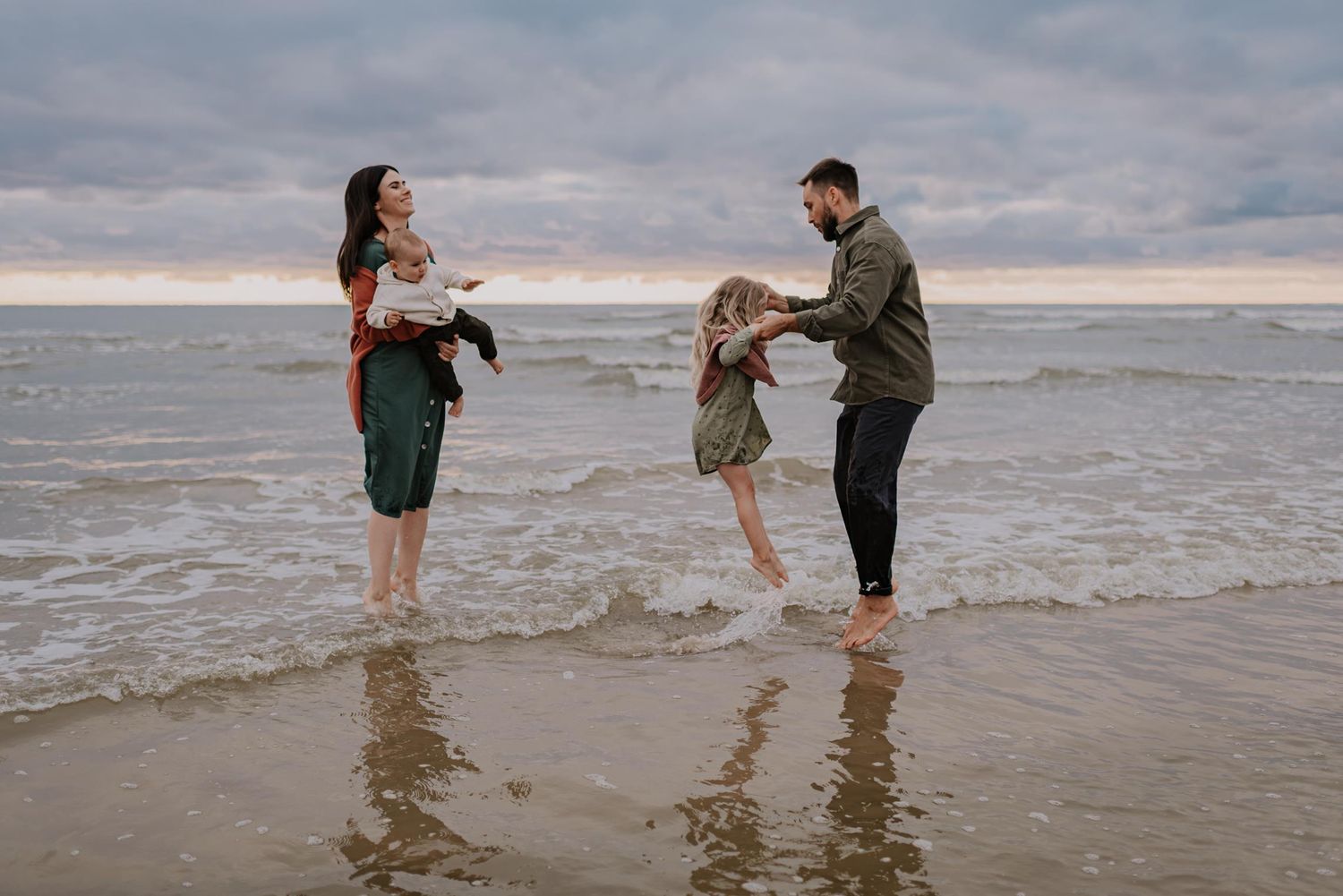 Family splashing and playing in ocean waves during beach photoshoot.